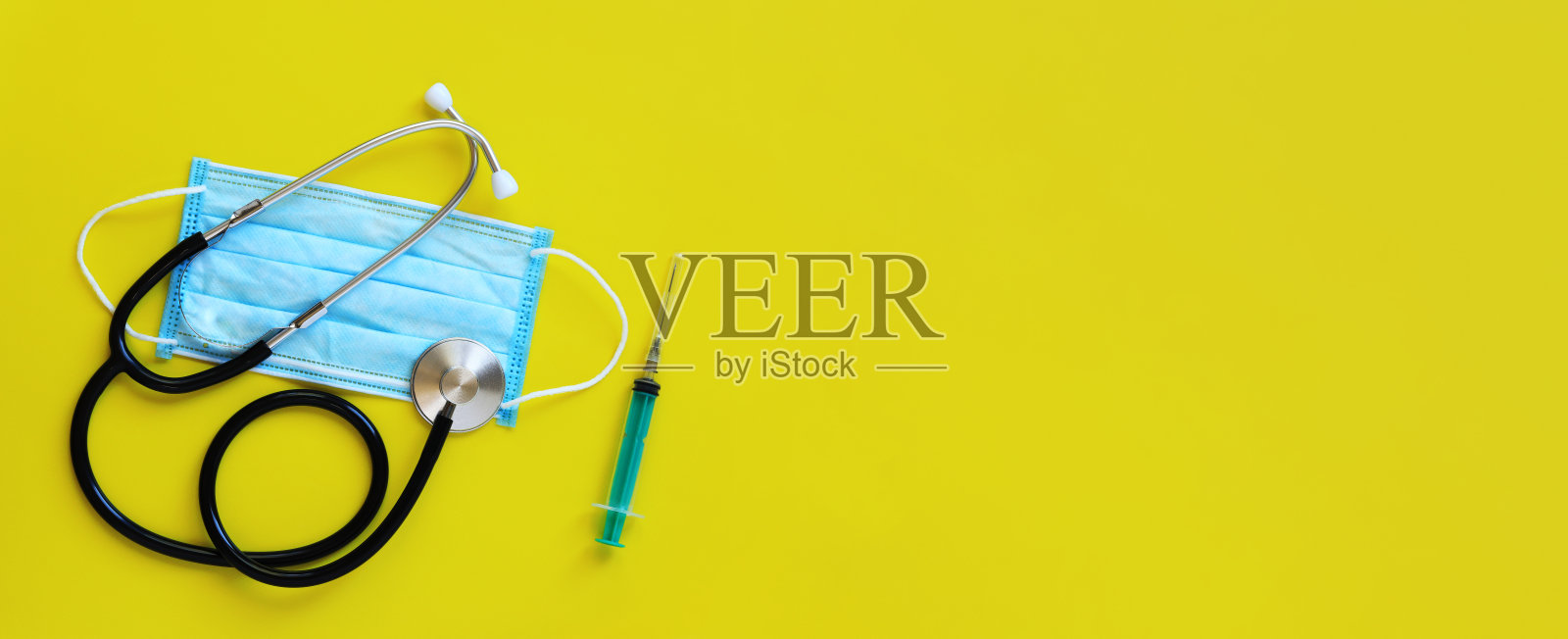 黄色背景的听诊器、医用防护口罩和注射器照片摄影图片