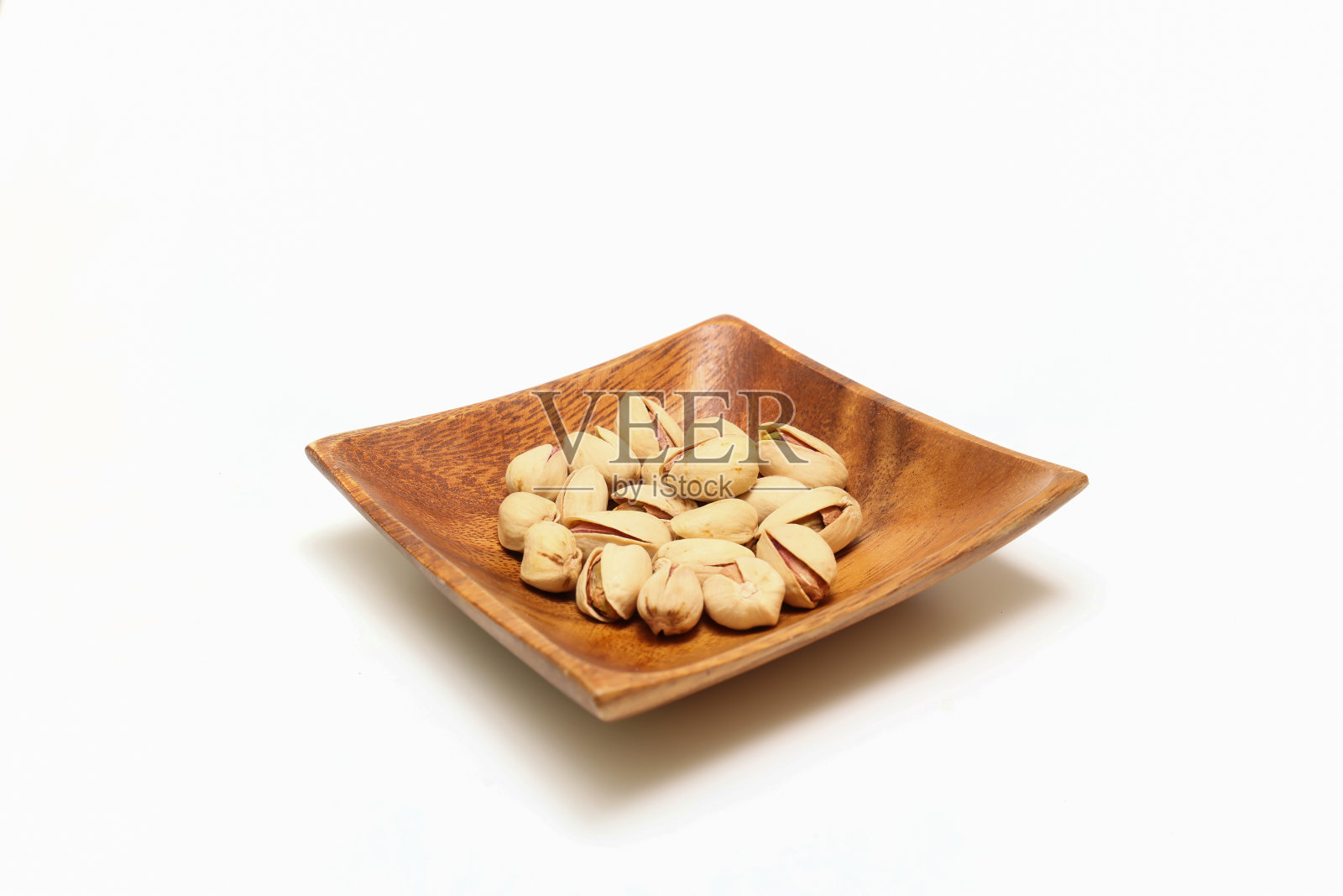开心果放在一个木制盘子上，孤立在白色的背景上。照片摄影图片