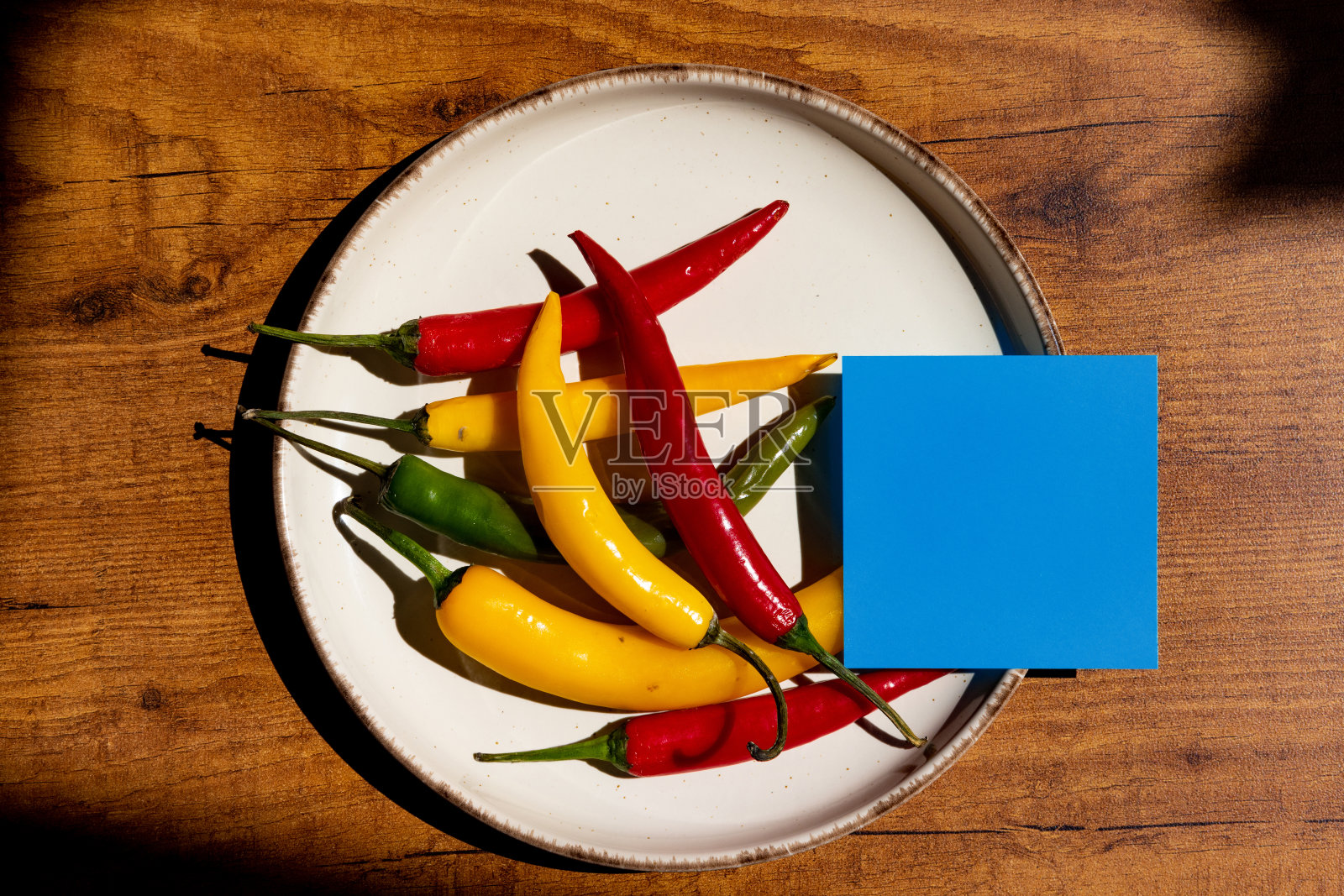 蓝色的便利贴放在白色的盘子上，上面放着红、绿、黄三种辣椒照片摄影图片