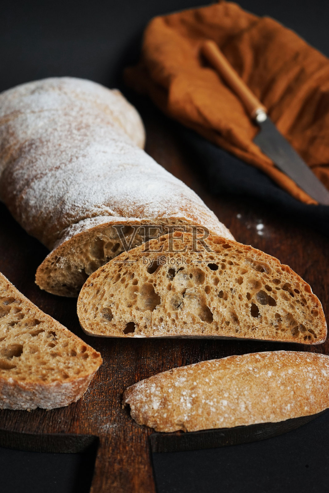 新鲜切片的面包放在木板上，旁边是一把刀和一张亚麻布餐巾照片摄影图片