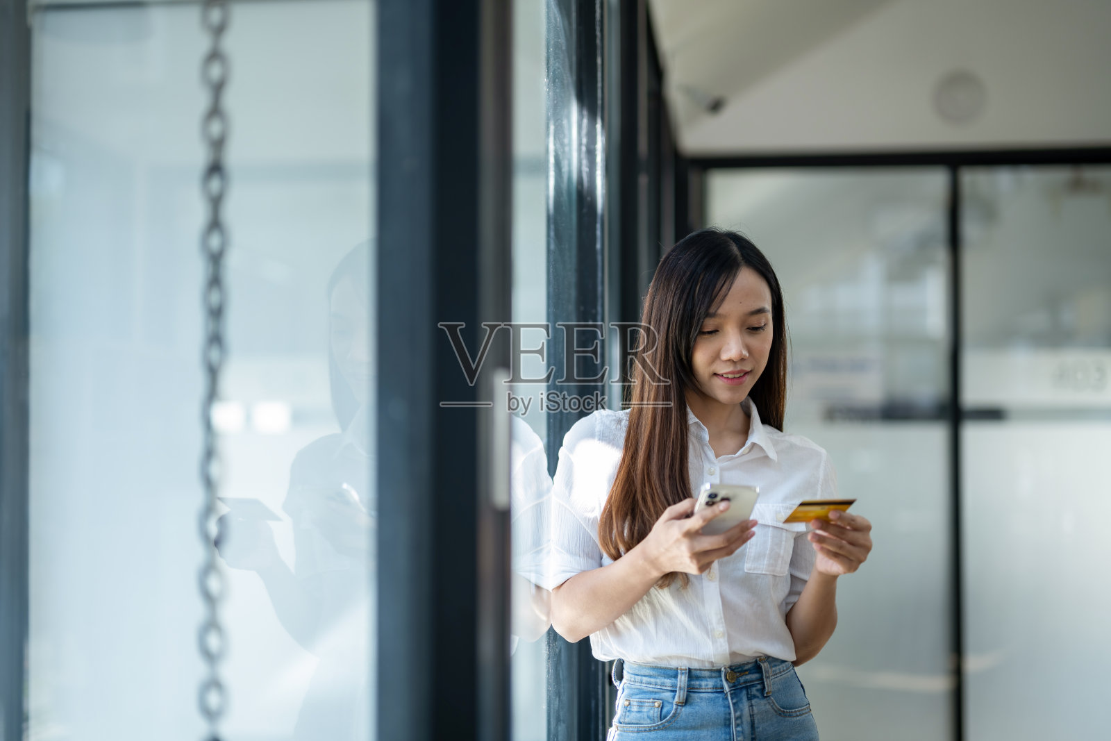 微笑的年轻女子用智能手机，拿着信用卡，可能在网上购物。照片摄影图片