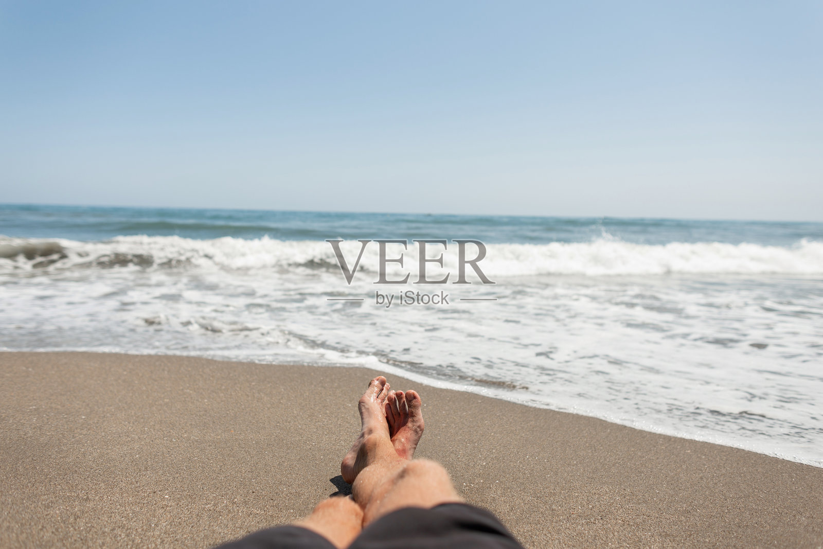 男人喜欢躺在沙滩上度假。在一个阳光明媚的日子里，一个人在蓝色的海边放松。自由职业者放松。时间放松。注意腿部。照片摄影图片