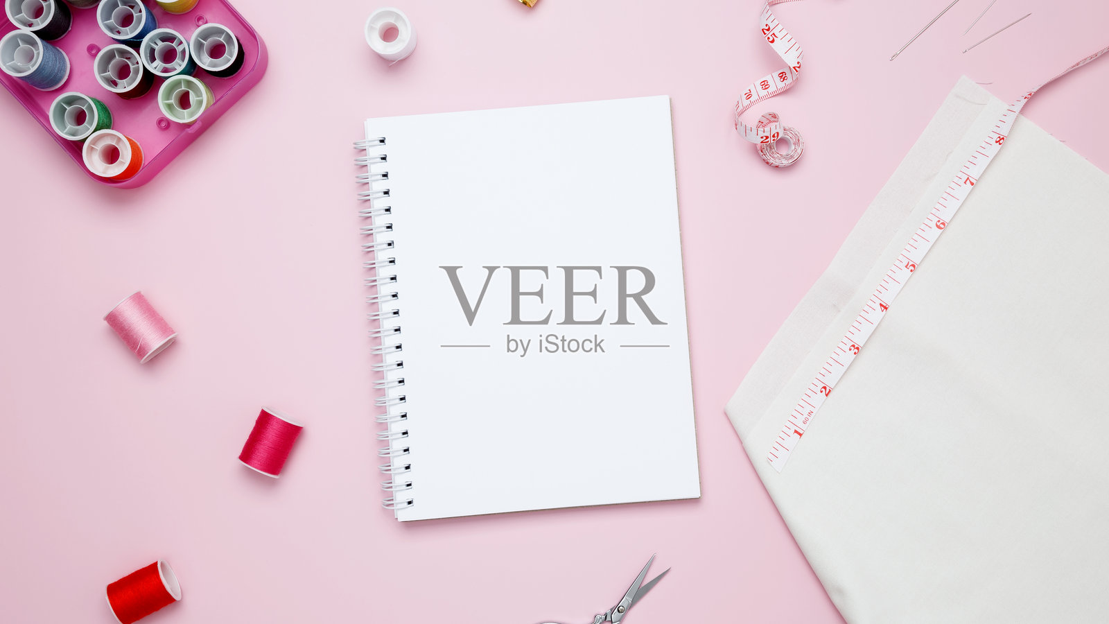 在粉红色的背景上用各种线和缝纫配件组成。模拟笔记本照片摄影图片