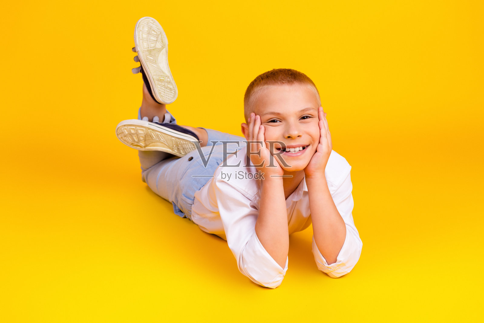 照片中开朗可爱迷人的男孩穿着白色衬衫放松休息地板孤立在黄色的背景照片摄影图片