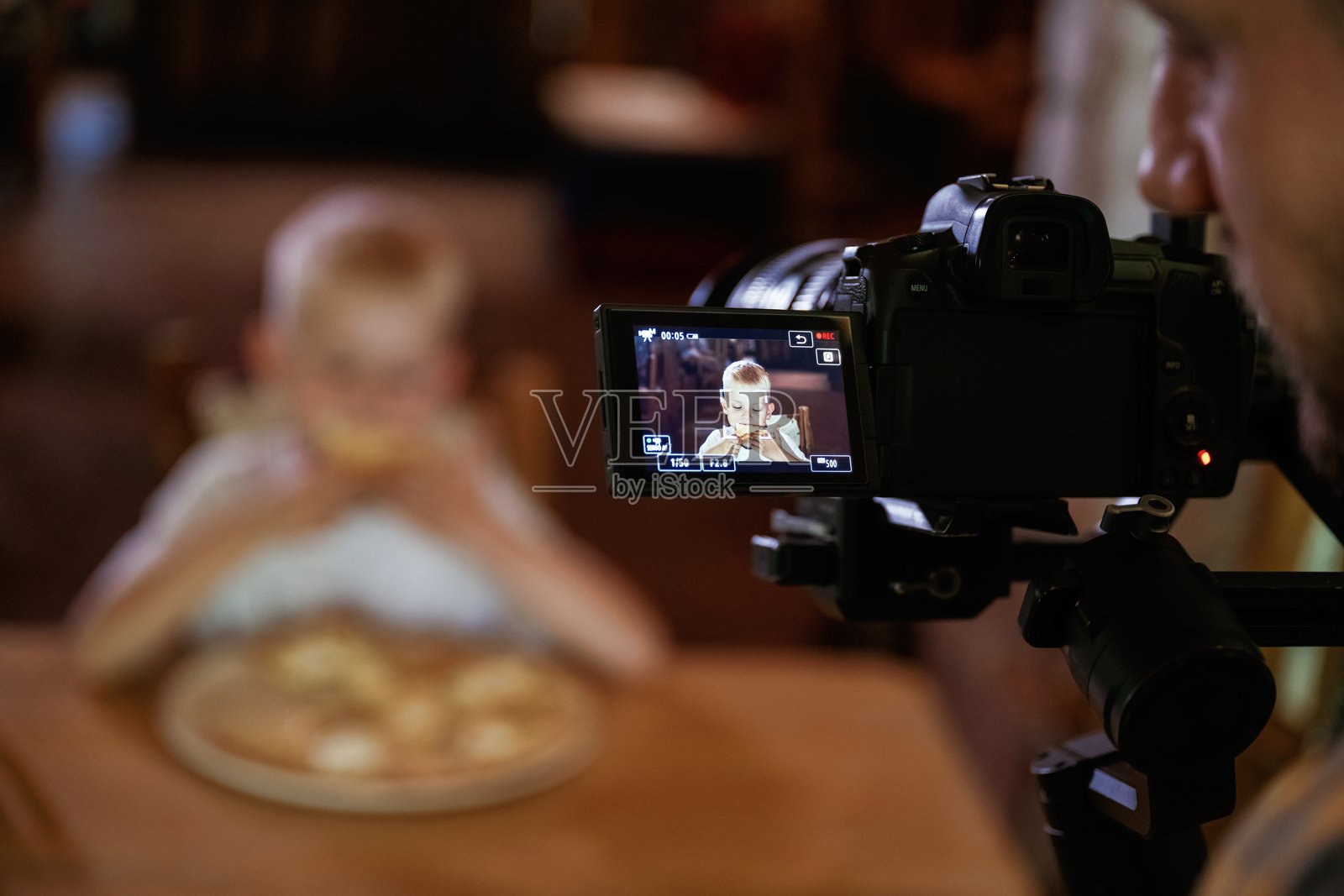 专业摄影师正在拍摄他。小男孩坐在室内吃着美味的披萨照片摄影图片