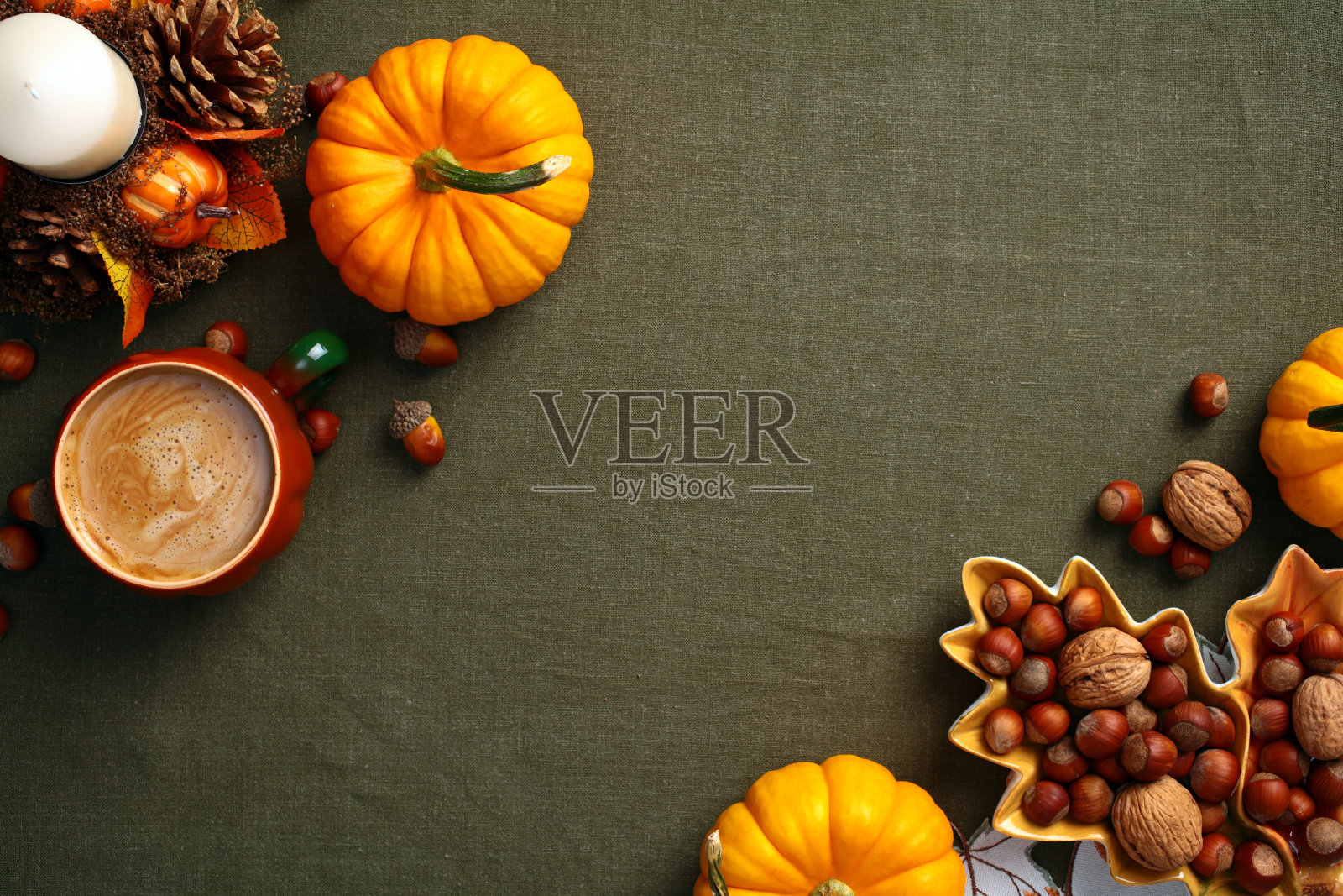 秋天的平面构图。橙色的南瓜，坚果，橡子，咖啡杯，老式绿色桌布上的蜡烛。俯视图秋季hygge风格的桌子照片摄影图片