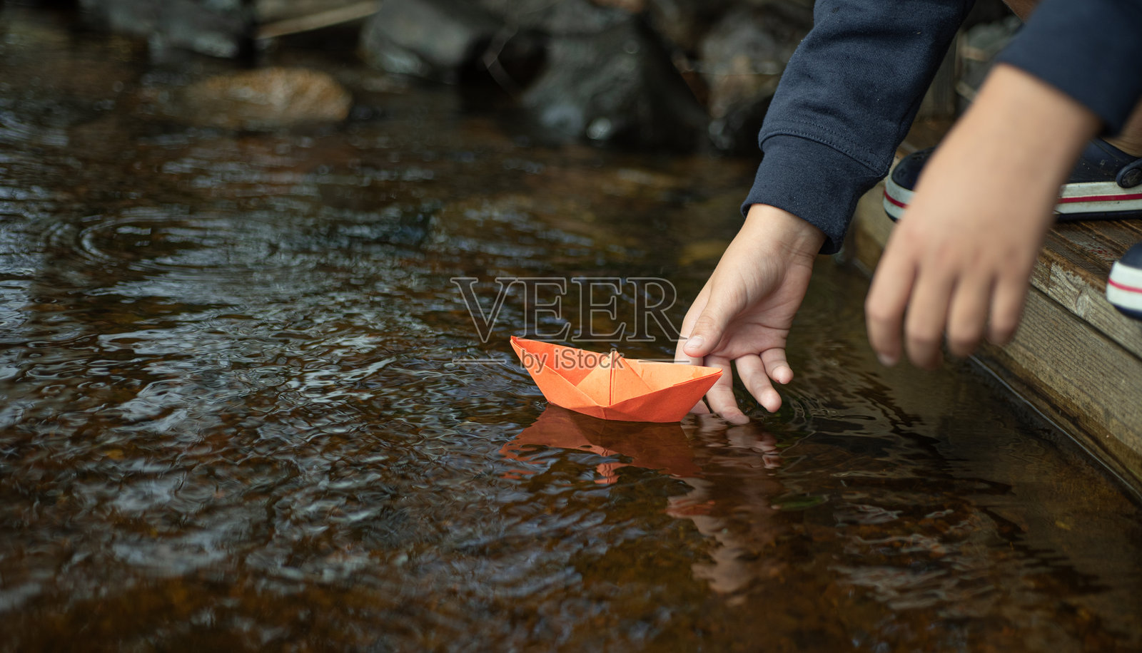 一个男孩把纸船放进水里照片摄影图片