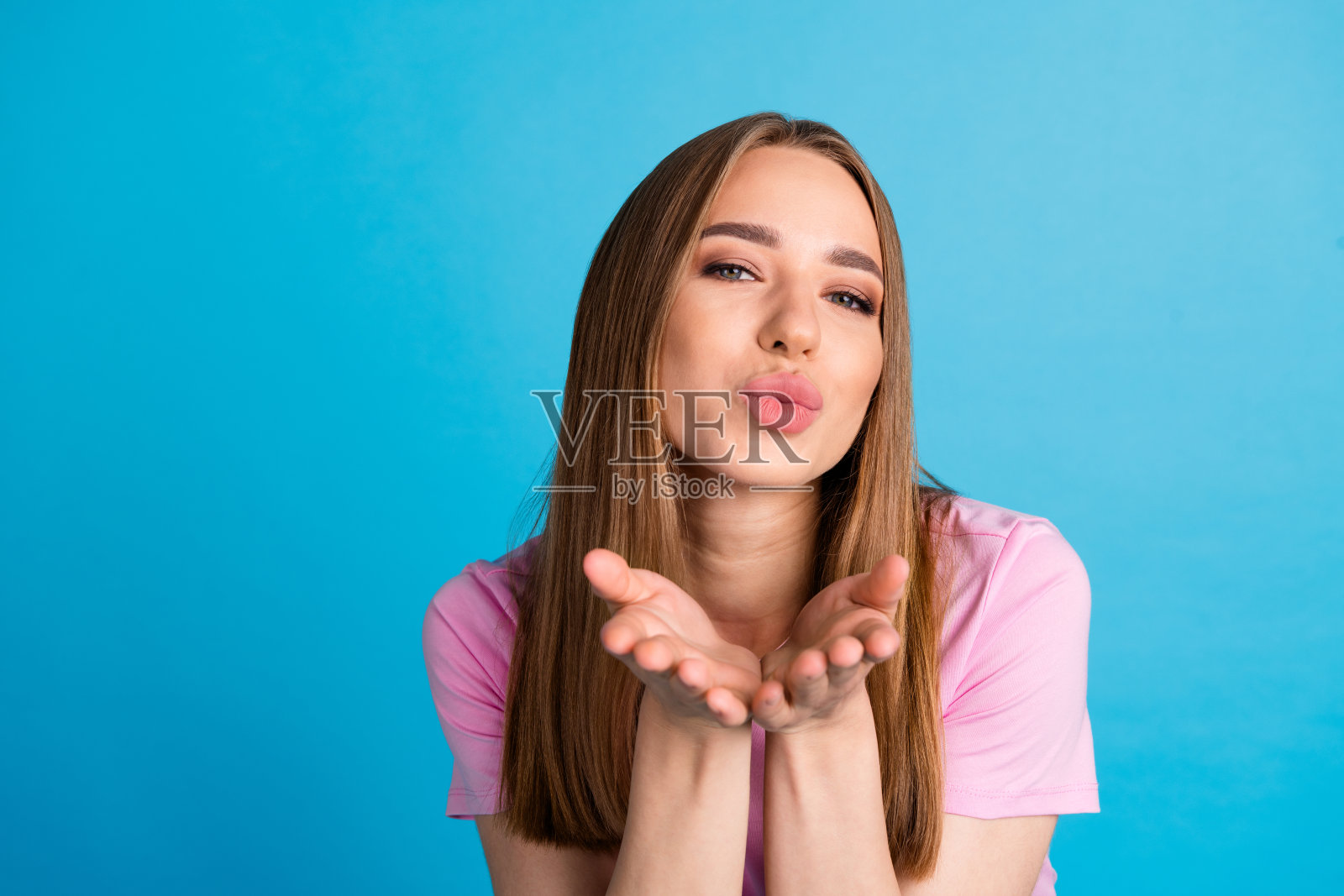可爱可爱的女人穿着时髦的粉红色衣服，在蓝色的背景上发出孤立的吻照片摄影图片