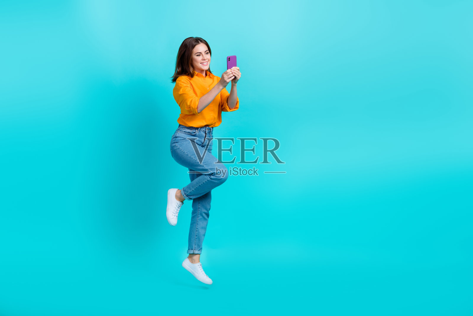 自信漂亮的女士全身照片穿橙色衬衫跳跃打字苹果三星设备孤立的绿松石色背景照片摄影图片