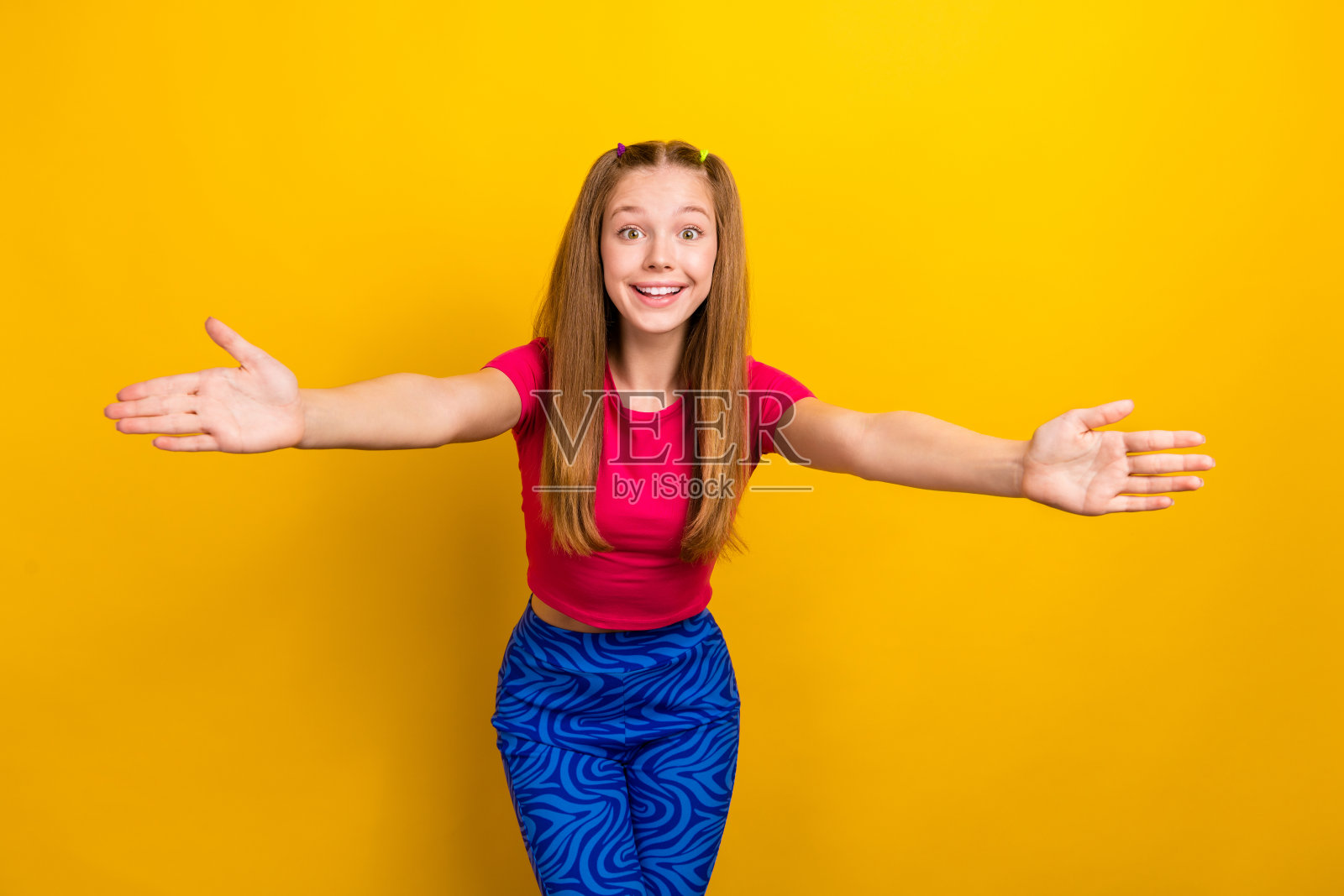 年轻的十几岁的女孩穿着复古的蓝色打底裤，粉红色时髦的露脐上衣，想拥抱朋友，问候孤立在黄色背景照片摄影图片