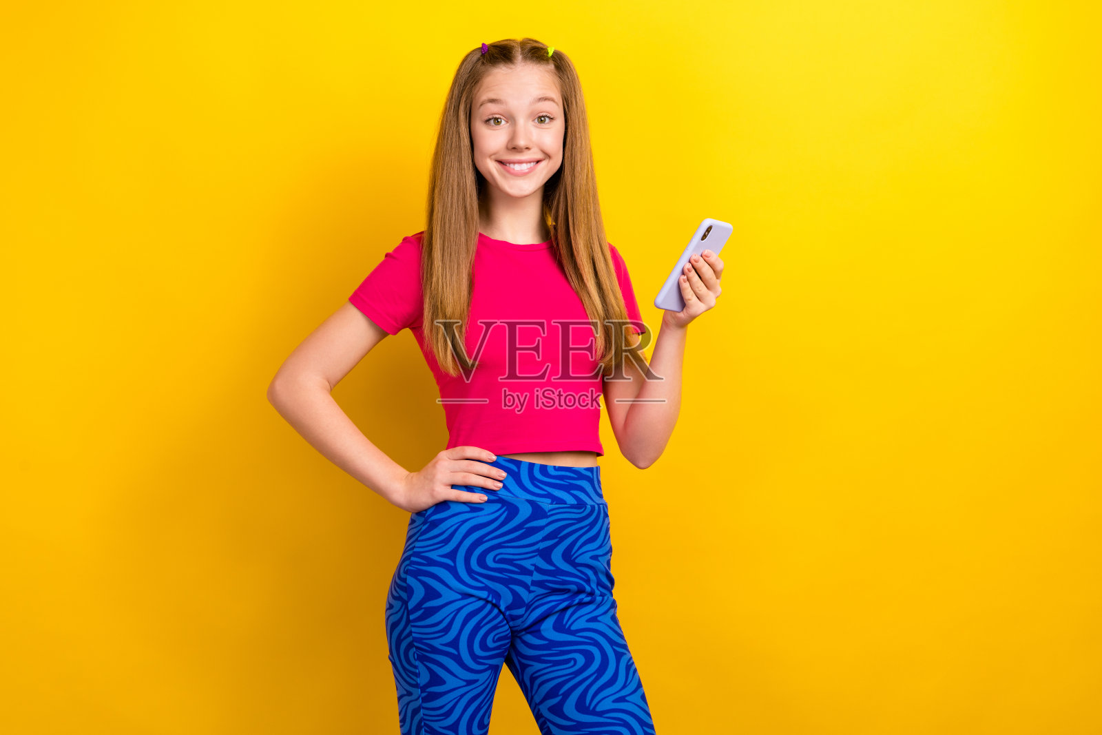 照片正面可爱漂亮的女学生直发，穿着粉红色的t恤，拿着智能手机孤立在黄色背景照片摄影图片