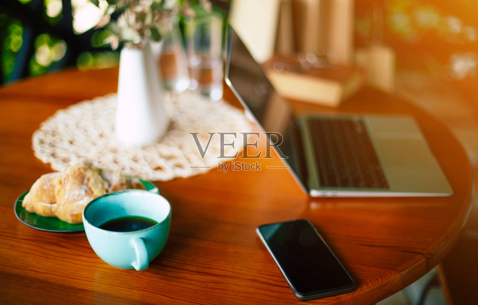 在咖啡馆的木桌上模拟笔记本电脑的空白屏幕，一杯咖啡饮料和新鲜的羊角面包，手机放在电脑旁边。自由职业者的工作空间照片摄影图片