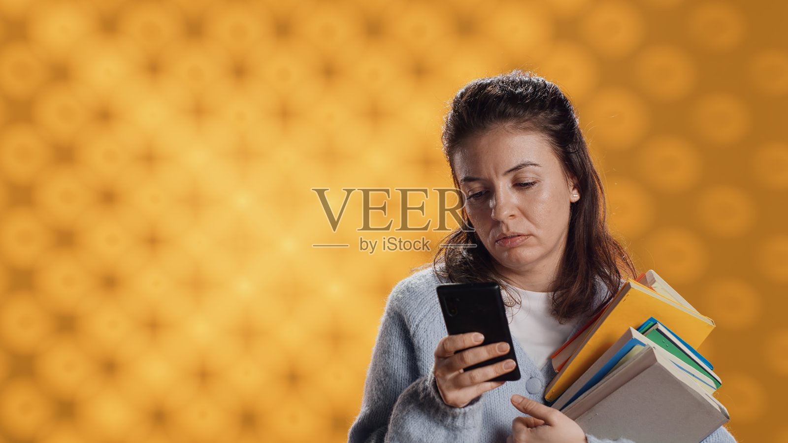 心烦意乱的女人拿着一摞书，用电话准备学校考试照片摄影图片