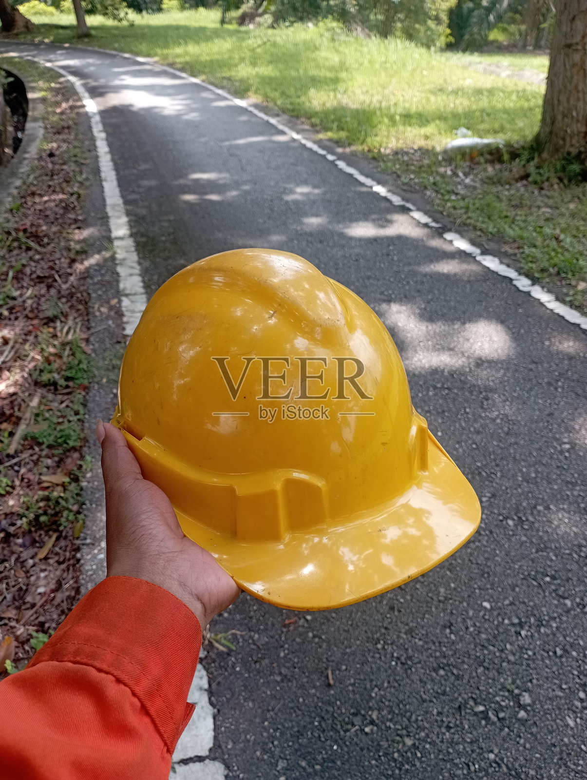 拿着承包商工人的黄色头盔，在室外的背景下照片摄影图片