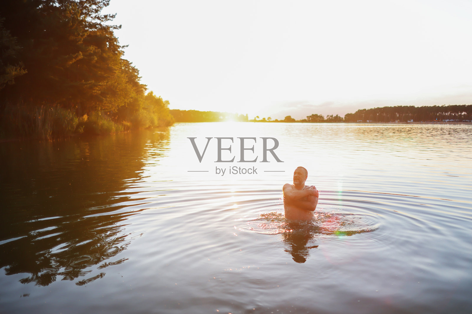 成熟的男人在日落时在湖中游泳照片摄影图片