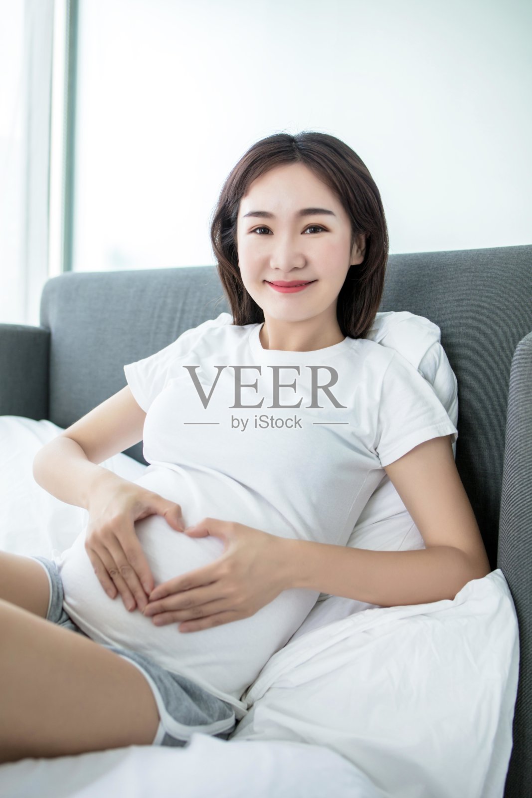 一名孕妇躺在床上，双手在腹部形成心形照片摄影图片
