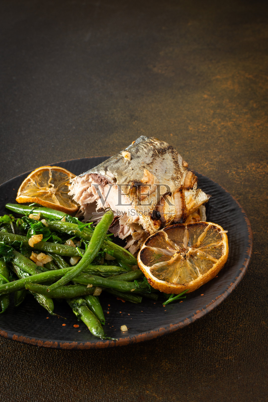 这道美味的菜肴以烤青豆、洋葱和嫩鲭鱼为特色，装在棕色背景的盘子里，提供一顿平衡而美味的美食照片摄影图片