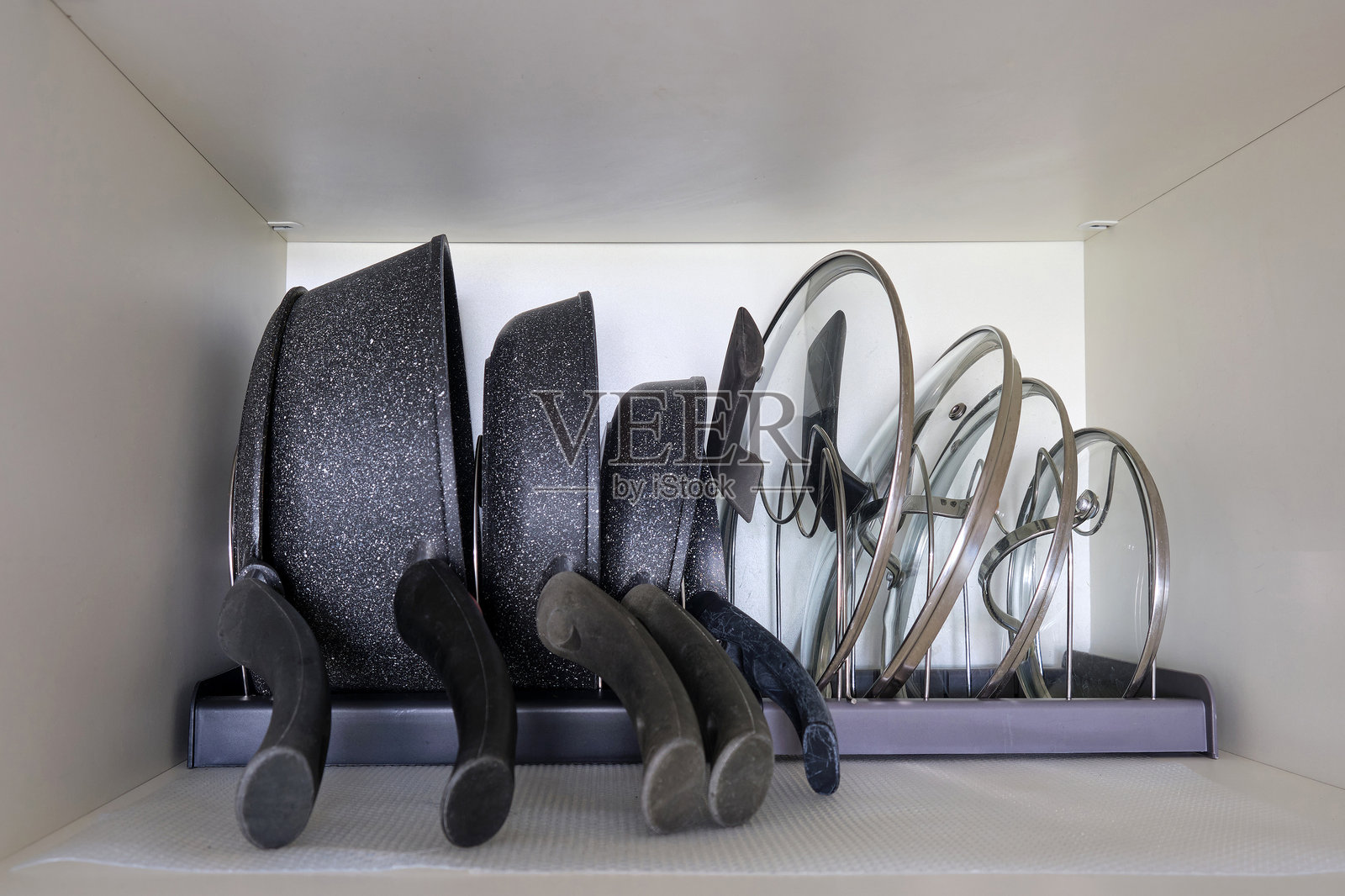 整理厨房里的餐具、锅碗瓢盆。在家庭厨房橱柜中使用锅和盖子的过程照片摄影图片