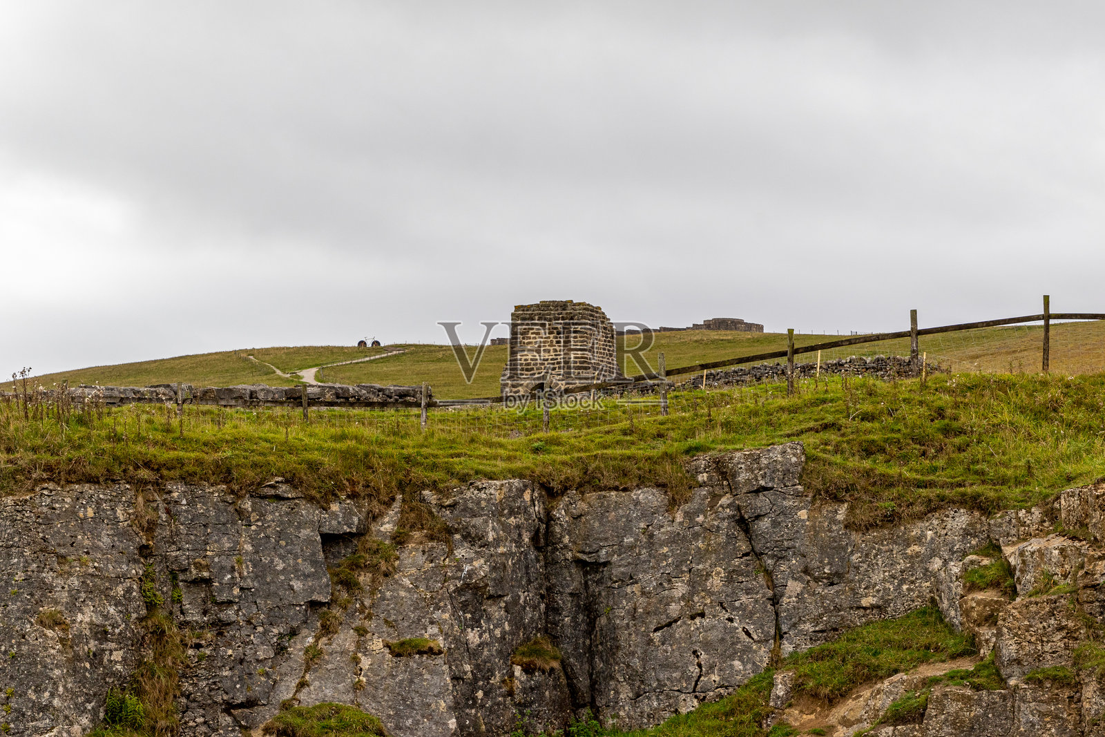 绿草如茵的小山上，阴云密布，质朴的石头结构，描绘了乡村景观和古建筑。照片摄影图片