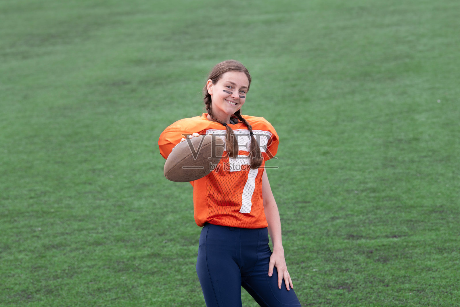 一个穿着美式橄榄球制服的女孩，背景是一片绿色的田野。照片摄影图片