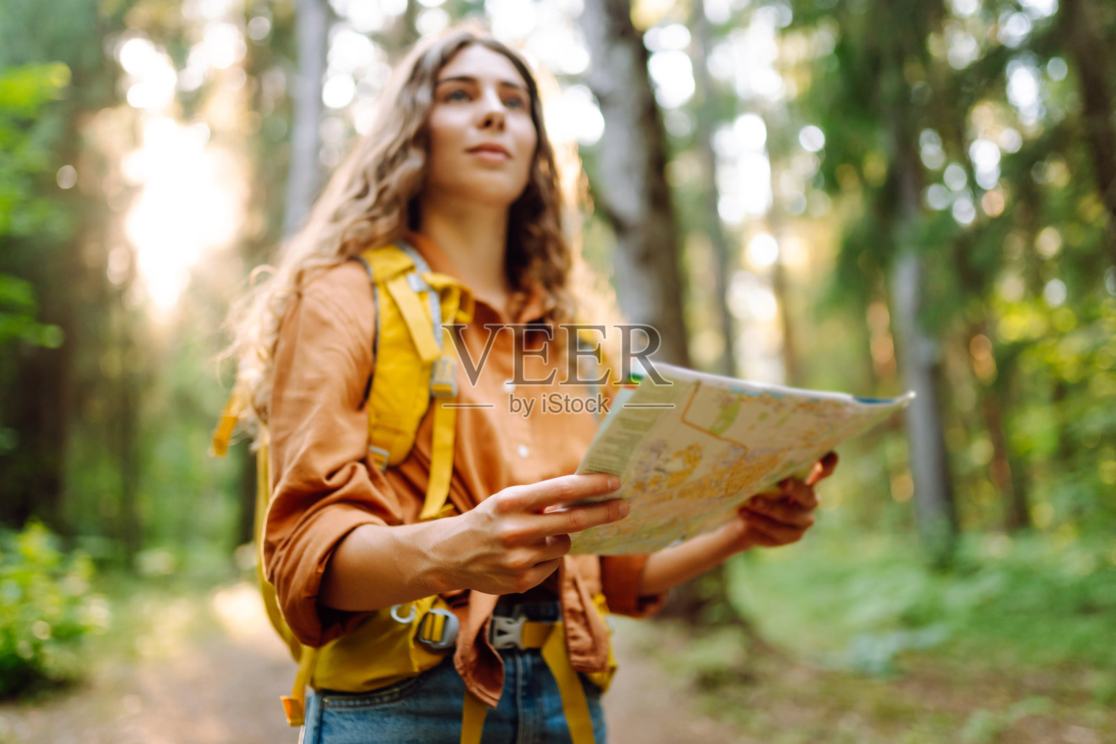 一位年轻女子一边在阳光下看地图，一边探索森林。照片摄影图片