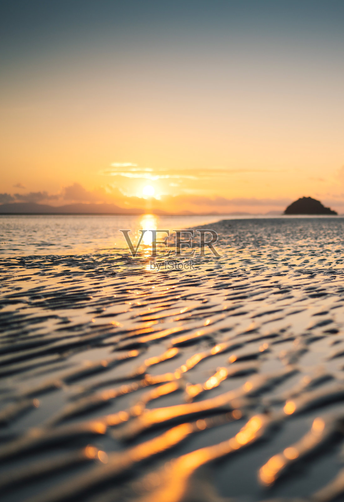 夕阳在平静的海面上投下温暖的光芒，在泰国南部普吉岛的水面上，涟漪轻轻地扭曲了它的倒影照片摄影图片