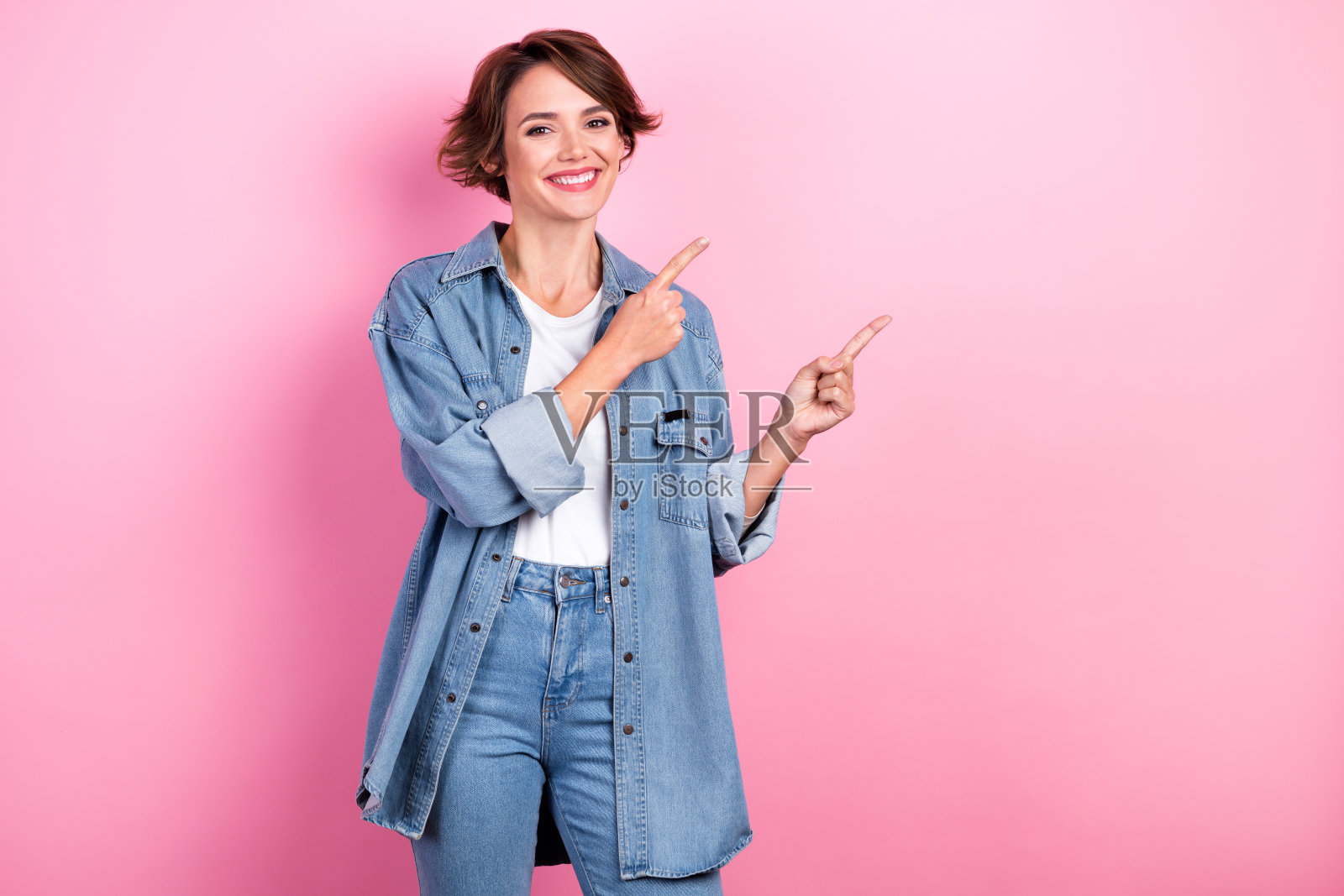 照片积极的促销员女士穿着牛仔牛仔裤服装，手指暗示模拟开放服装品牌销售季节孤立在粉红色的背景照片摄影图片