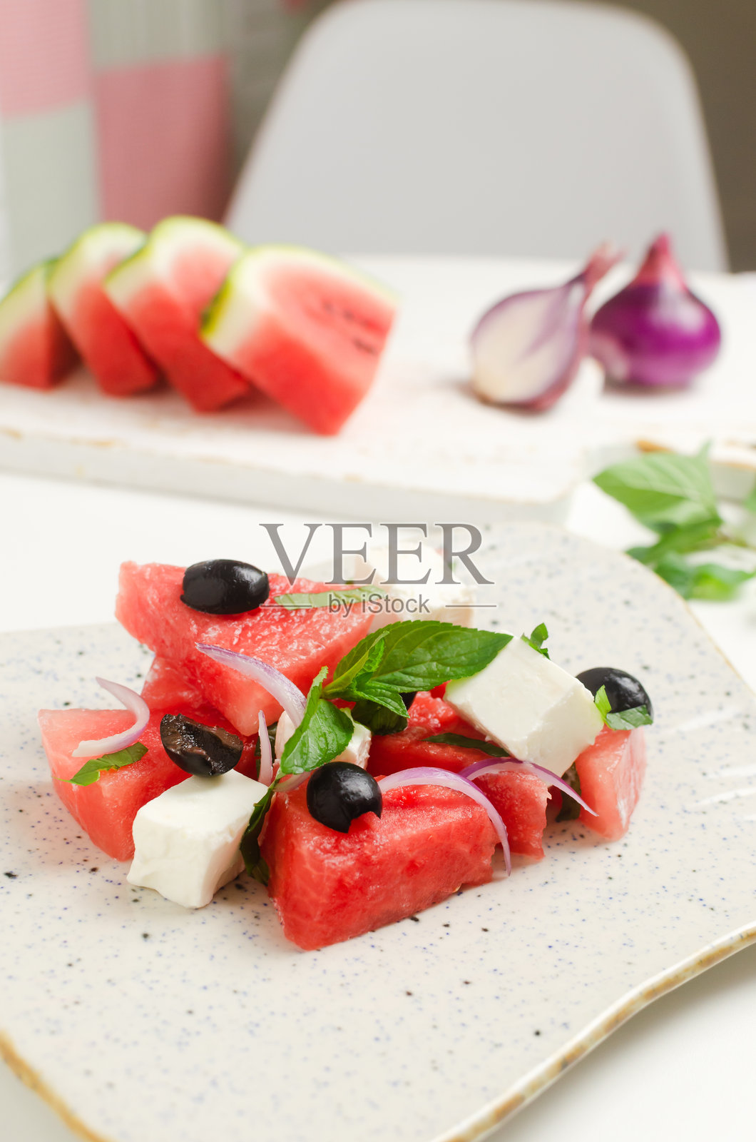 夏日沙拉，西瓜，羊乳酪，橄榄和薄荷装在白色的盘子里，放在白色的桌子上，上面放着配料。健康饮食的概念。素食,素食者。垂直方向照片摄影图片