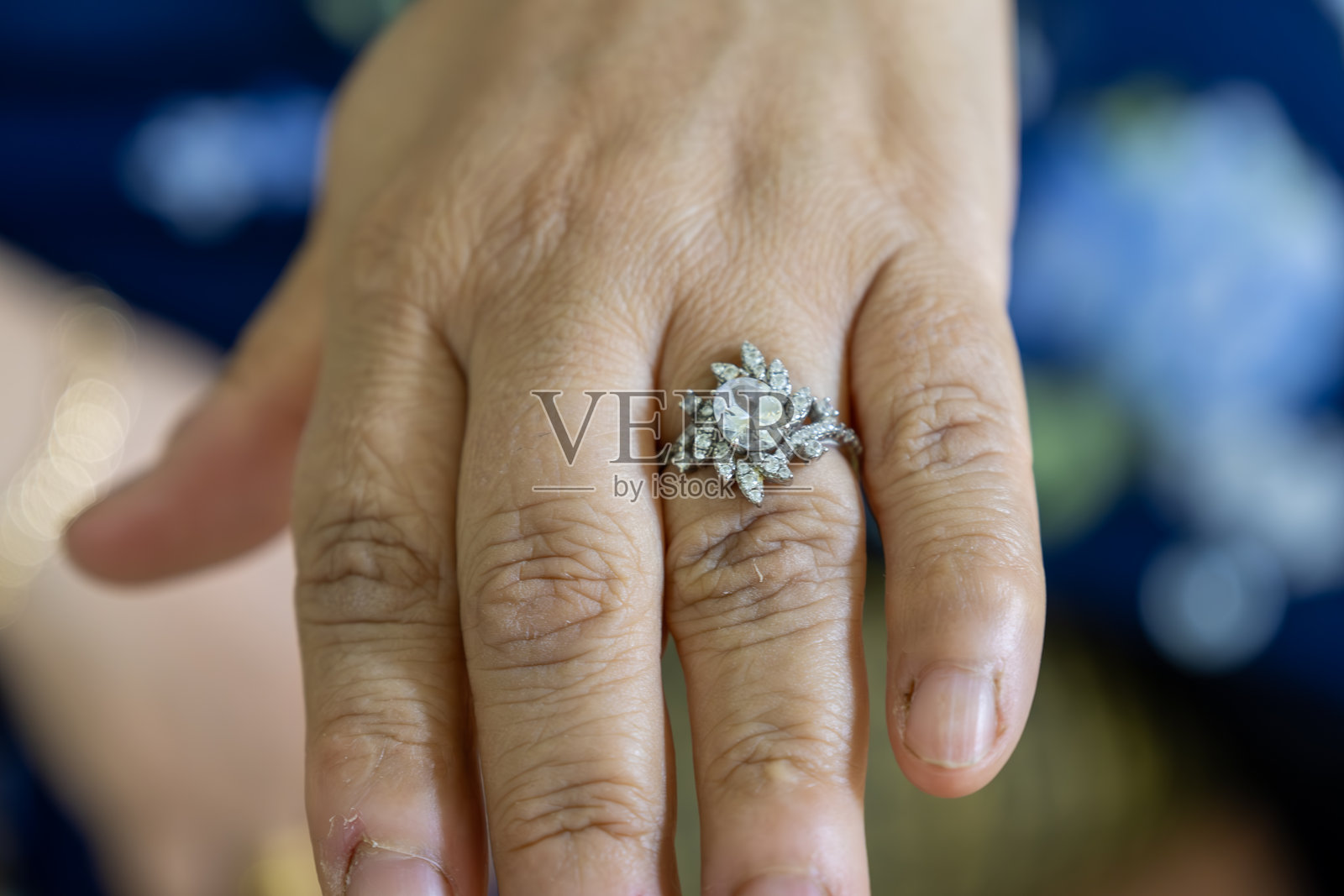 蓝色背景上佩戴闪耀钻石戒指的手部特写，象征着爱、承诺和永恒之美，非常适合婚礼或订婚照片摄影图片
