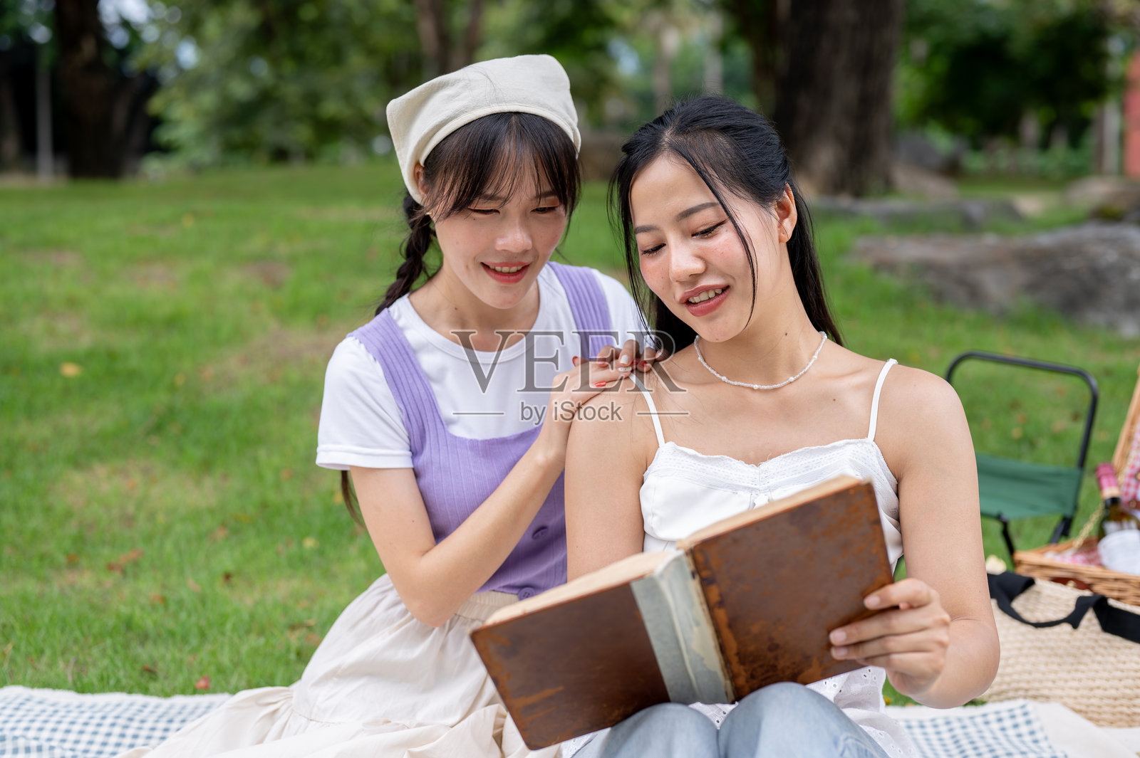两个美丽而积极的亚洲朋友在公园野餐时一起看书。照片摄影图片