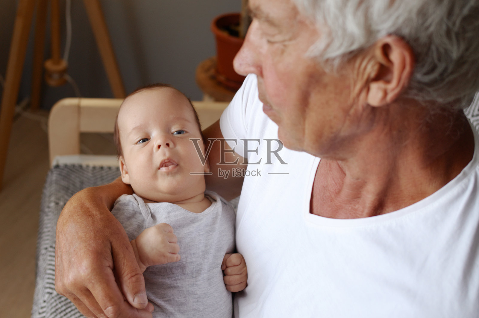 祖父怀里平静的婴儿。穿着白t恤的退休老人在家里抱着刚出生的孩子照片摄影图片