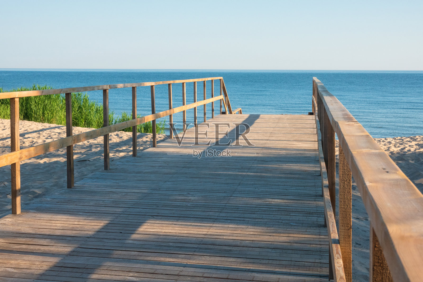 沿着一条穿过沙丘的木板路望去。在远处，你可以看到平静的大海和万里无云的天空。景观照片摄影图片