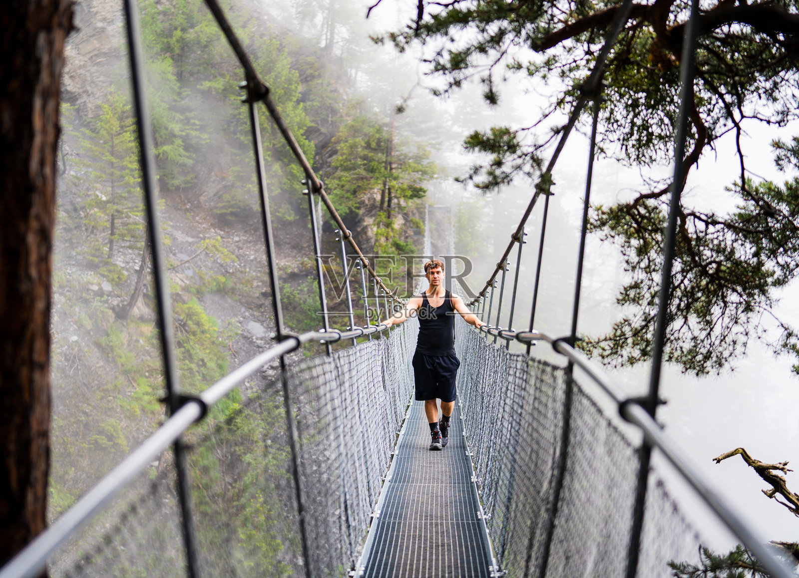 冒险的概念，一个人通过悬索桥，看着相机。照片摄影图片
