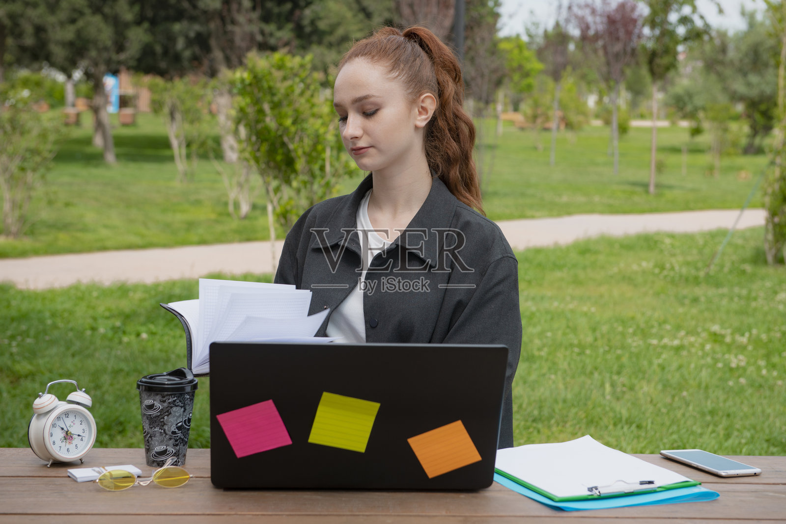 漂亮的年轻女子坐在户外的桌子旁，打开笔记本。照片摄影图片