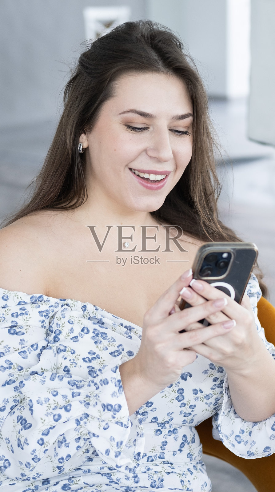 年轻漂亮的女人坐在演播室里拿着手机聊天。她在模特旁边工作时休息一下。幸福的脸，白色的背景。用智能手机给朋友发短信，滚动新闻。照片摄影图片