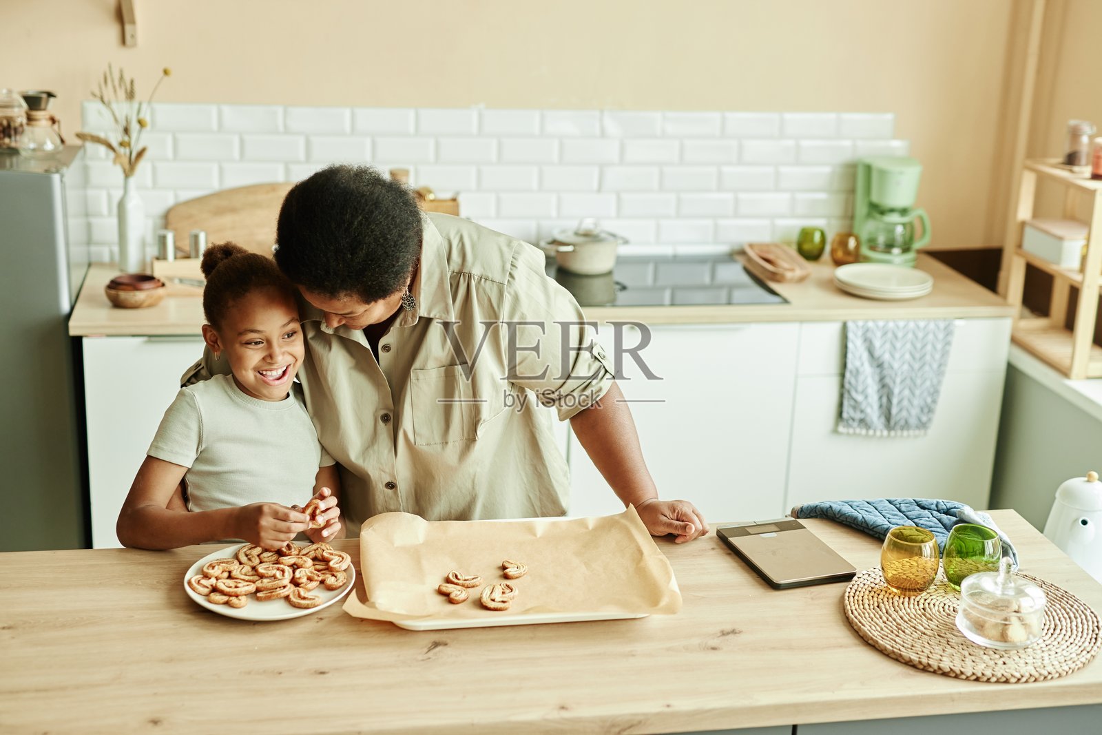 年长的黑人妇女拥抱在厨房做饼干的孙女照片摄影图片