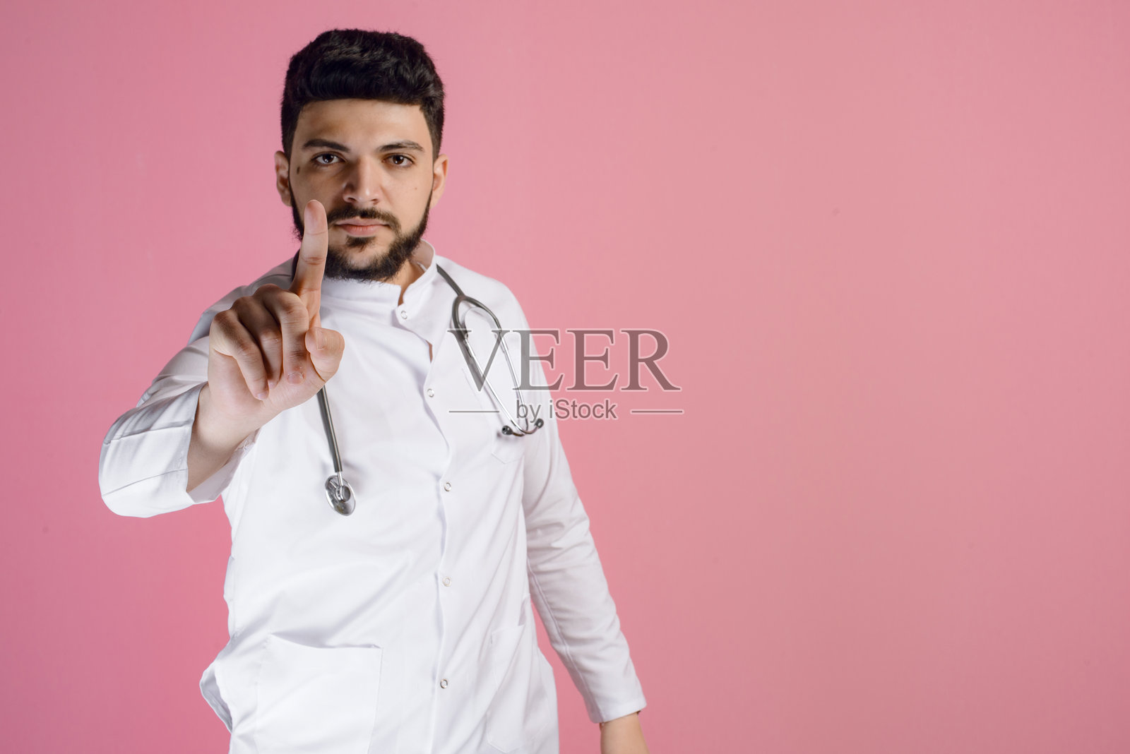 黑发医生，治疗师，内科医生，护理人员站着，看着镜头，举起手指。照片摄影图片