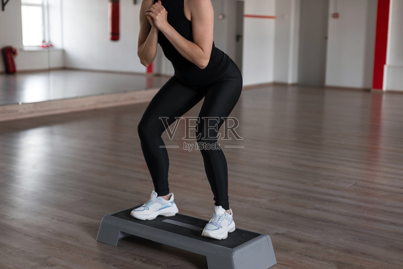 穿着黑色运动服的苗条运动的年轻女子蹲站在健身房的月台台阶上。女孩在做早操。健康的生活方式。特写镜头。照片摄影图片