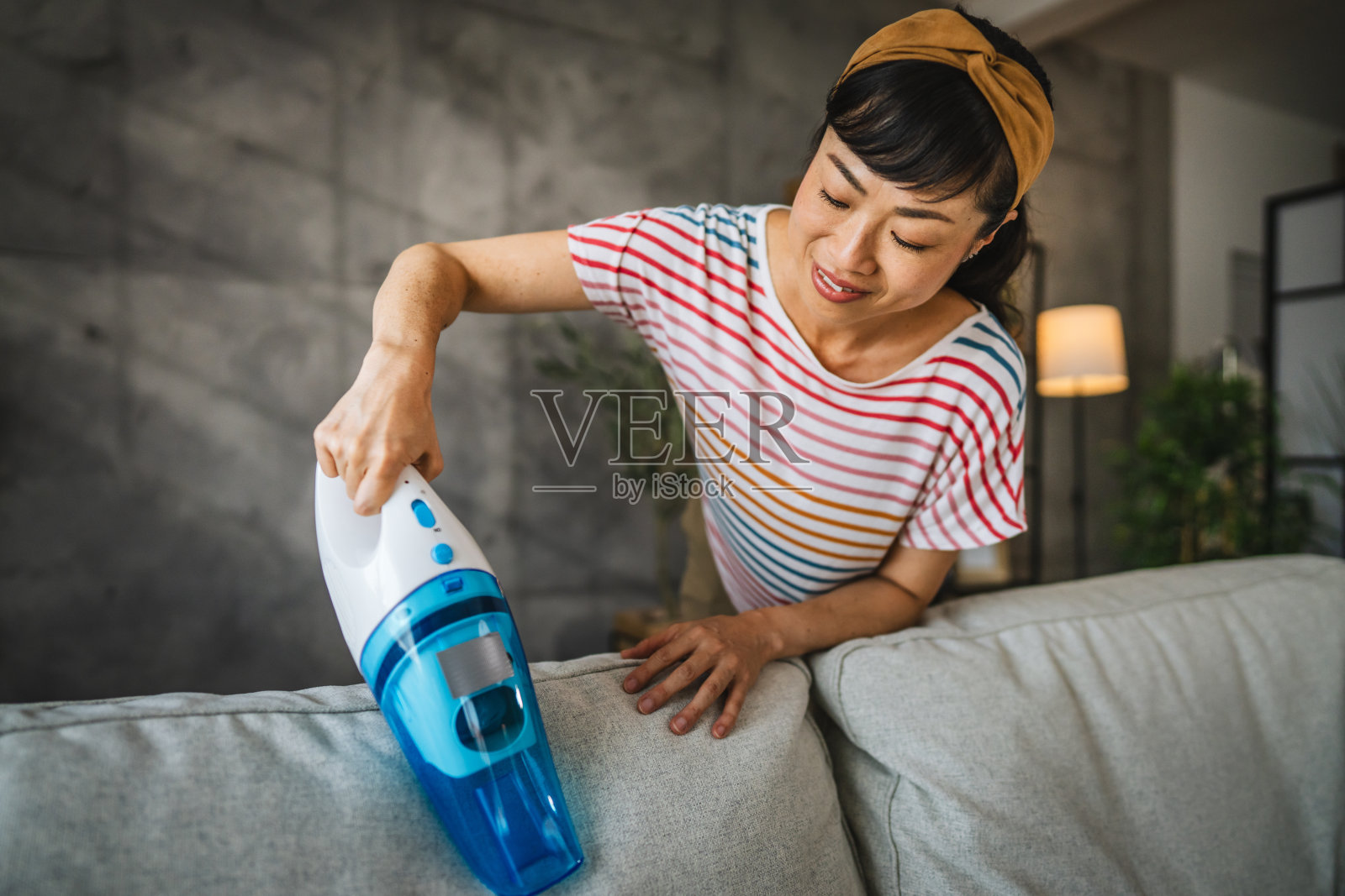 成熟的日本女人在家里用手吸尘机吸尘沙发照片摄影图片