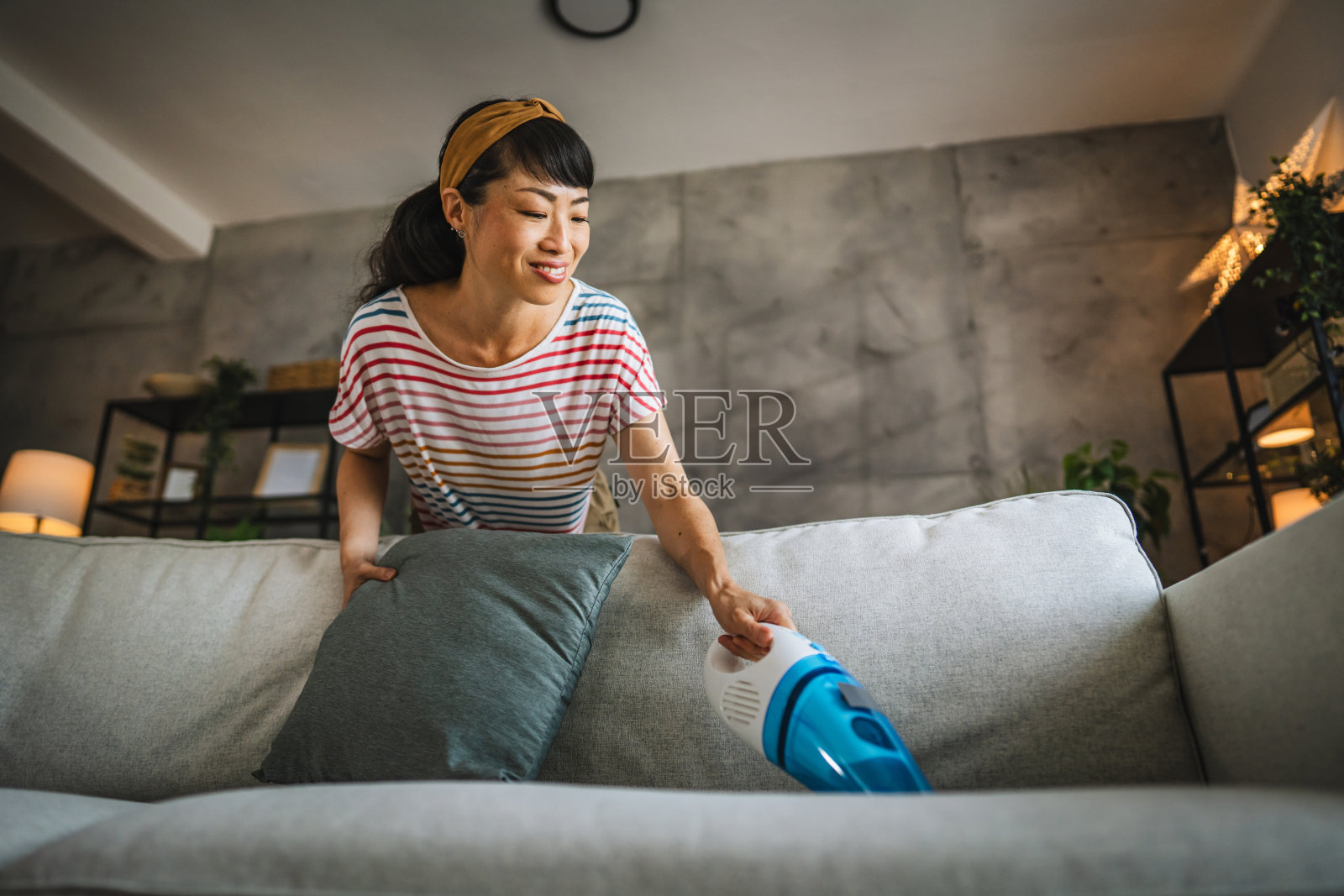 成熟的日本女人在家里用手吸尘机吸尘沙发照片摄影图片
