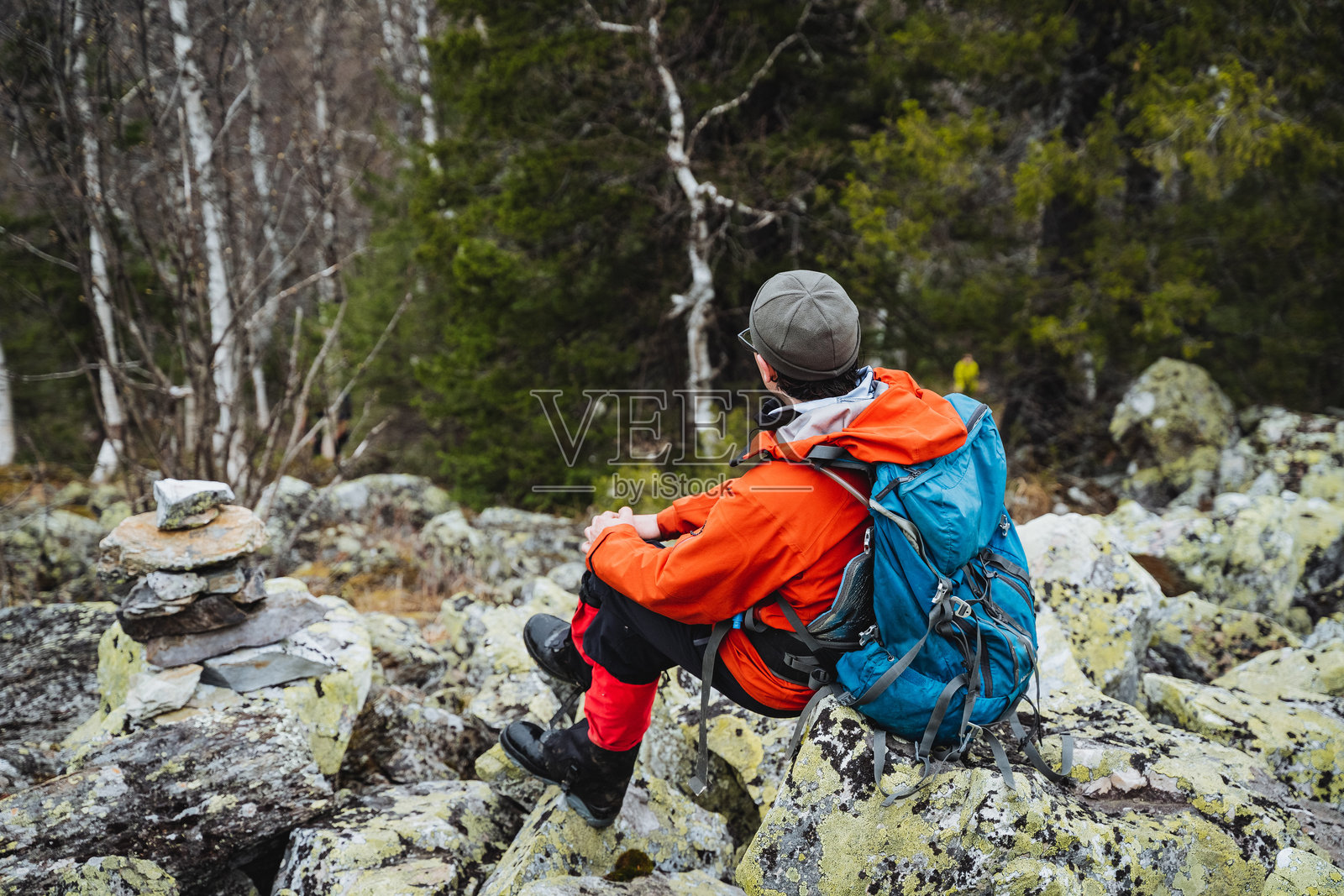 一个戴着帽子的男人坐在森林里的基岩上，享受着大自然的休闲时光照片摄影图片