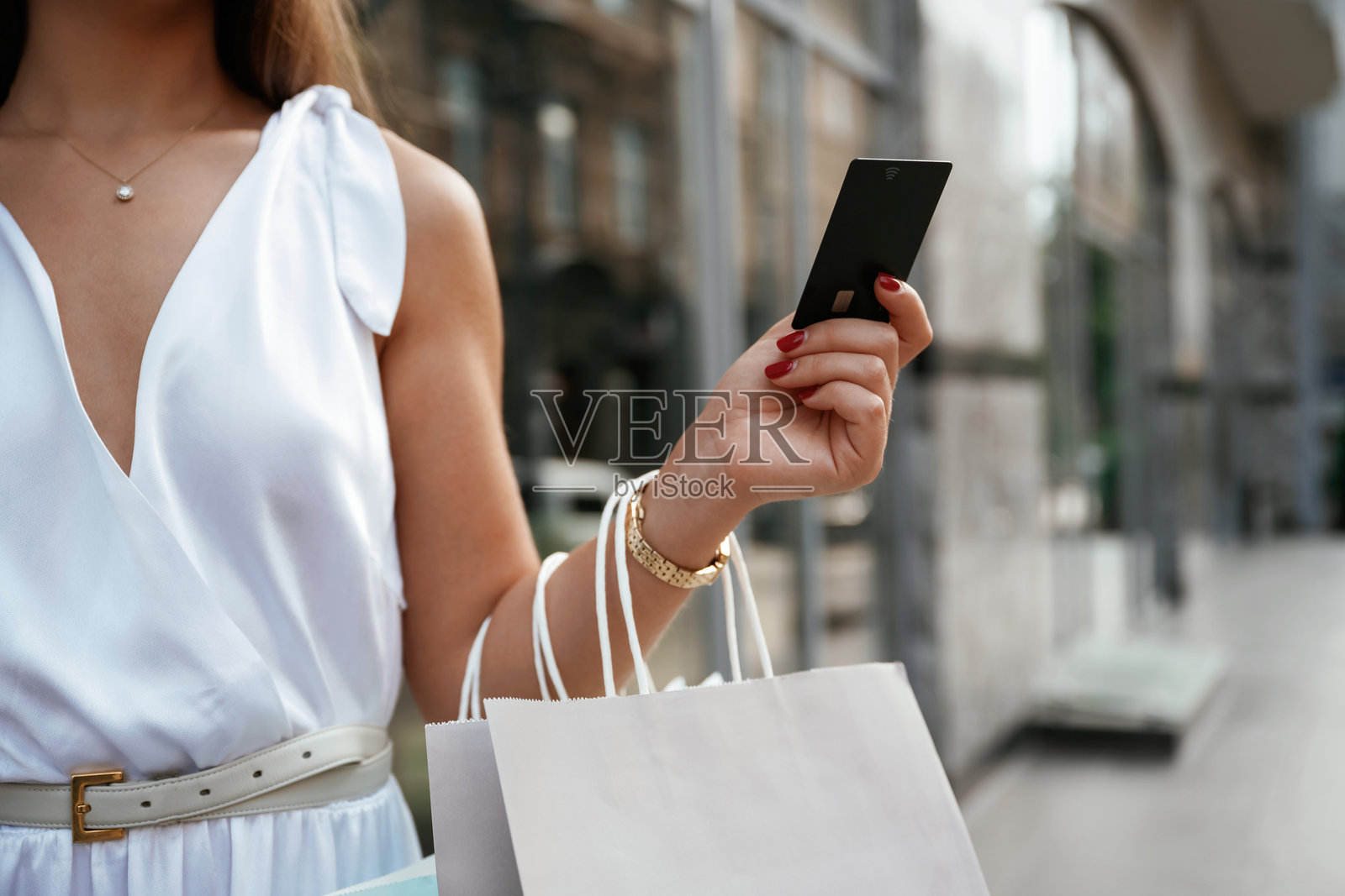 信用卡在手。一个时髦的女人拿着购物袋在大楼附近的户外照片摄影图片