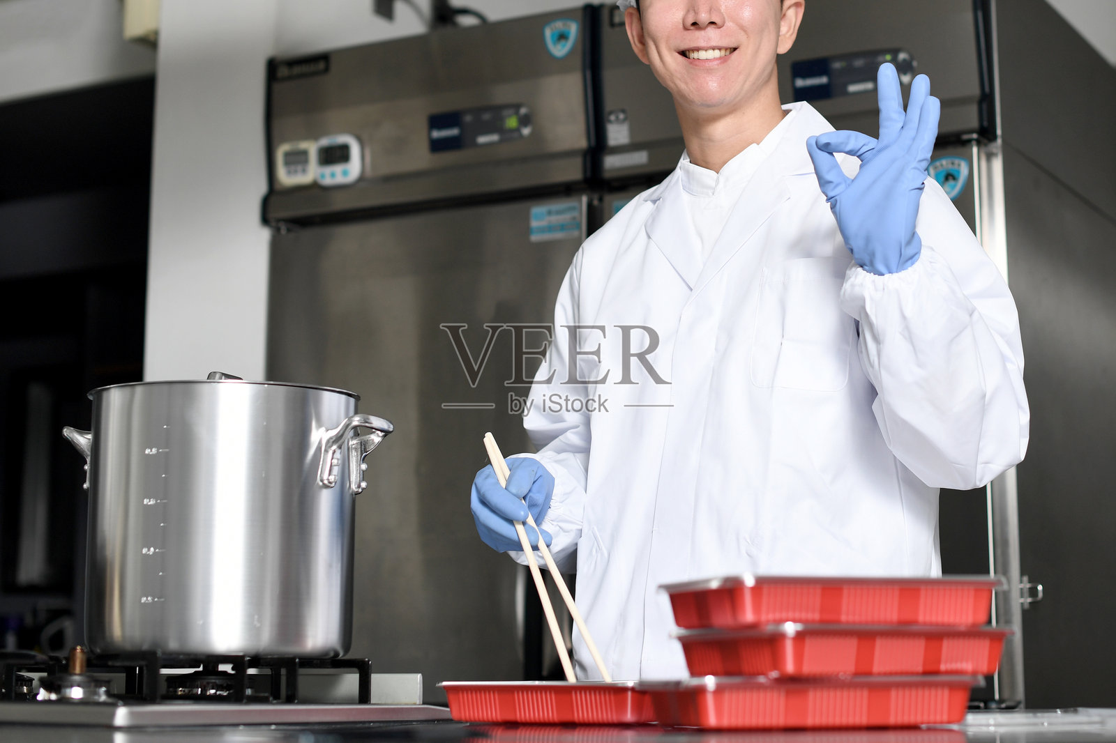 一名穿着干净西装的男厨师一边往便当盒里装食材，一边摆好姿势。照片摄影图片