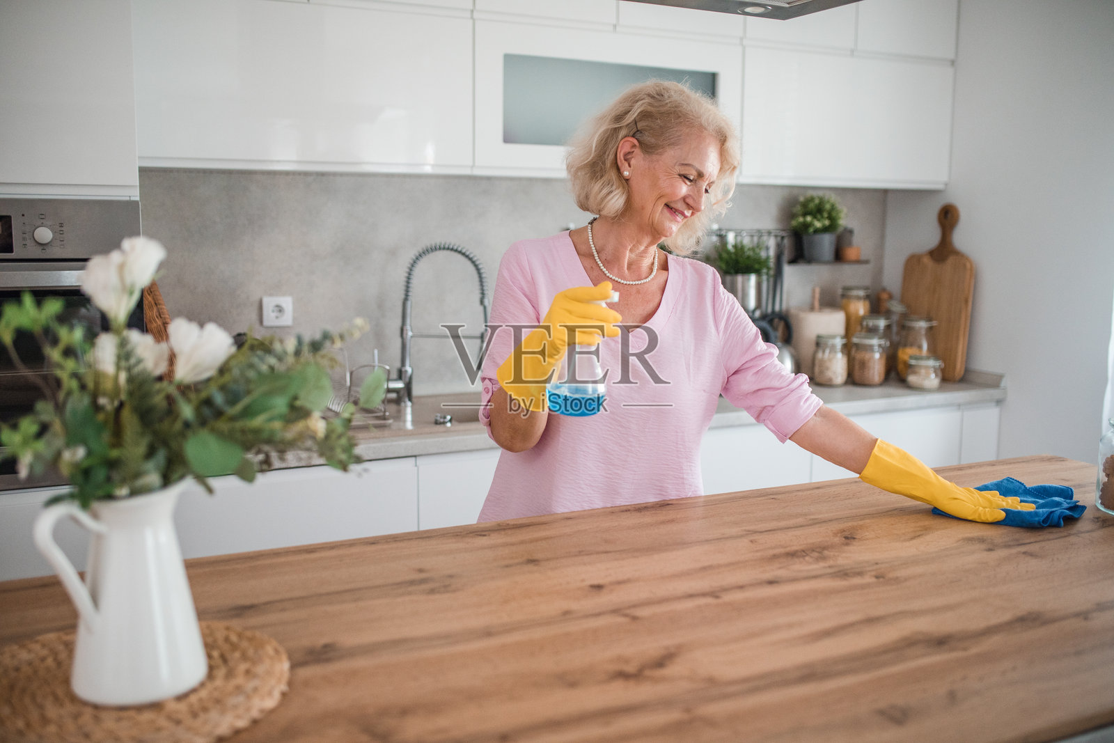 开朗的老年妇女喷洒厨房柜台，并使用木质表面清洁喷雾进行清洁照片摄影图片