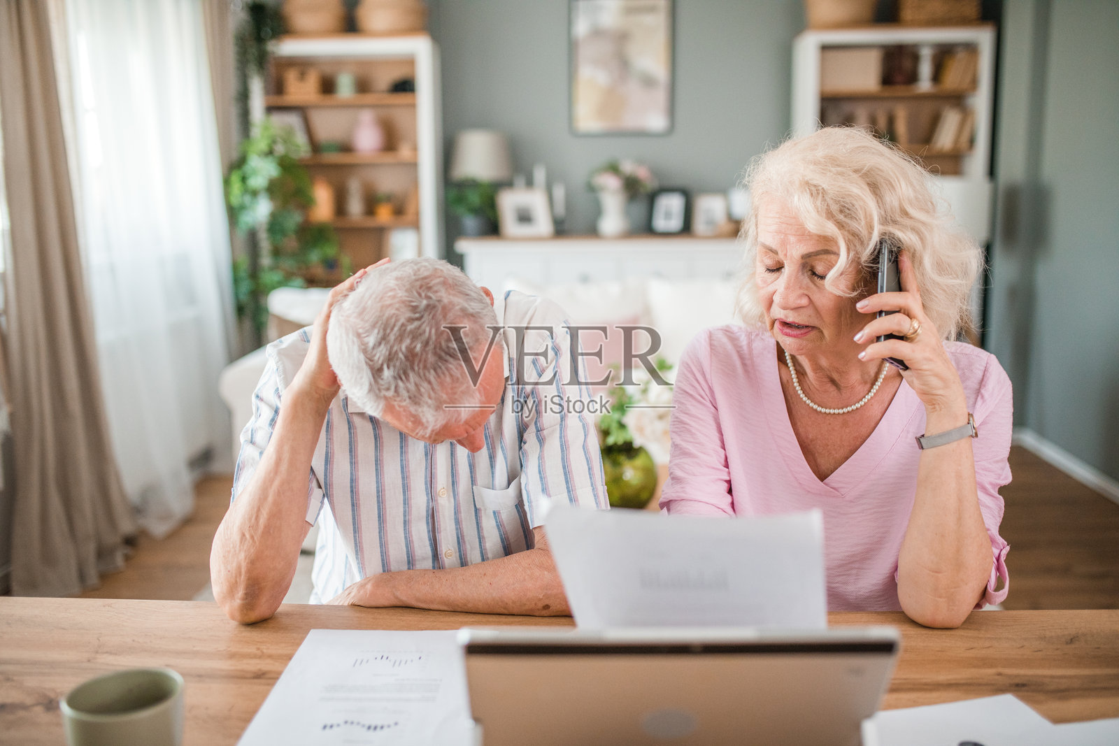 一位老妇人正在用手机和银行通话。她和忧心忡忡的丈夫正在经历他们必须处理的经济问题照片摄影图片