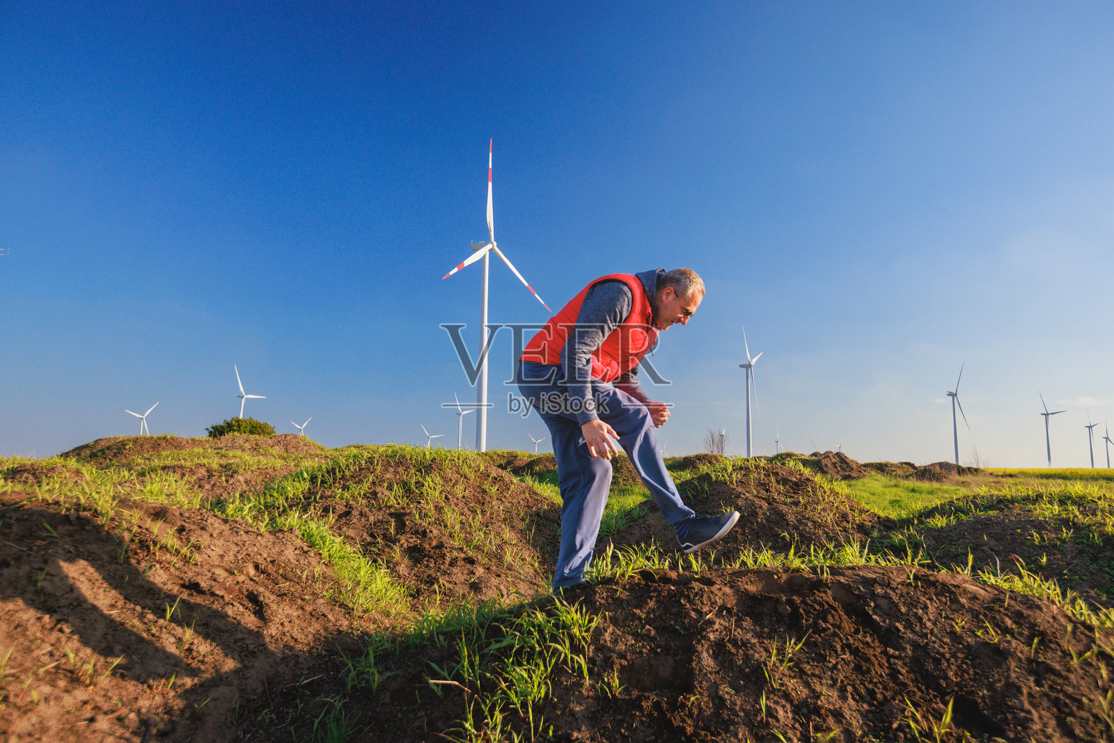 成熟的男人在山上跳跃，在农田与风电场照片摄影图片