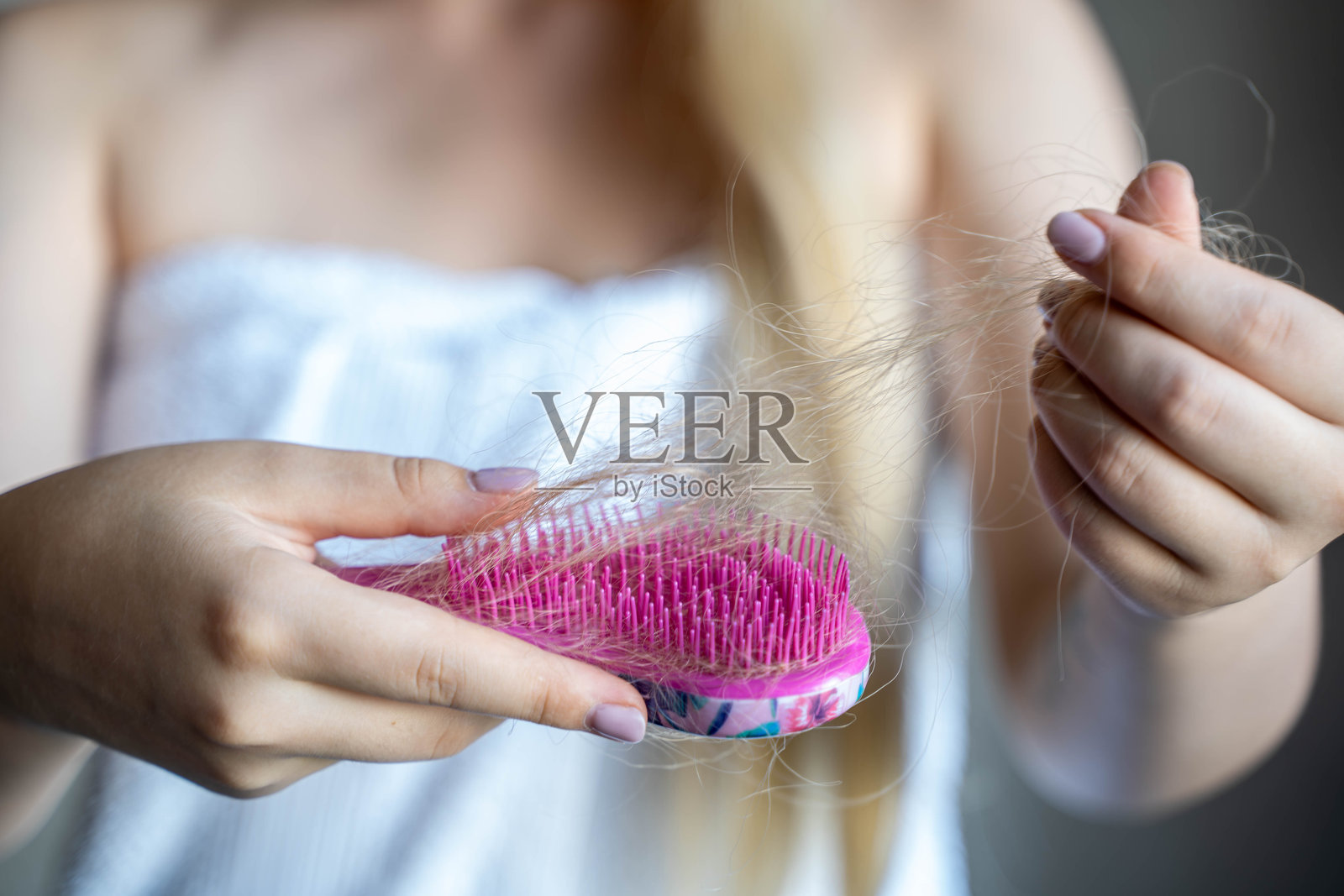 一个女人的特写，她拿着一把粉红色的梳子，里面装满了头发。照片摄影图片