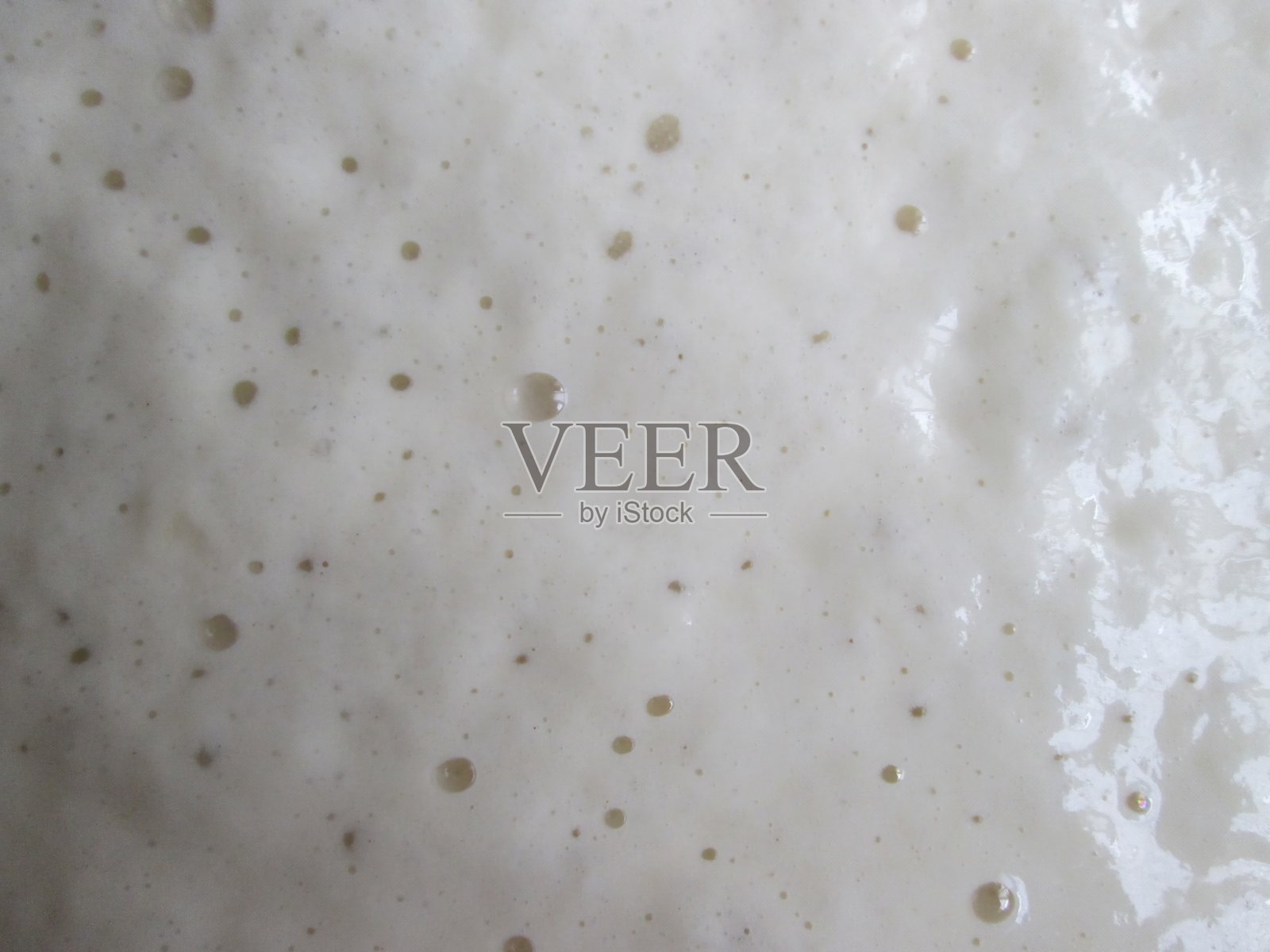 一个冒泡的酵母发酵剂的特写镜头，展示了它的泡沫质地和活跃的发酵过程，拍摄于早上一个温暖的厨房，突出了面包的准备过程。照片摄影图片