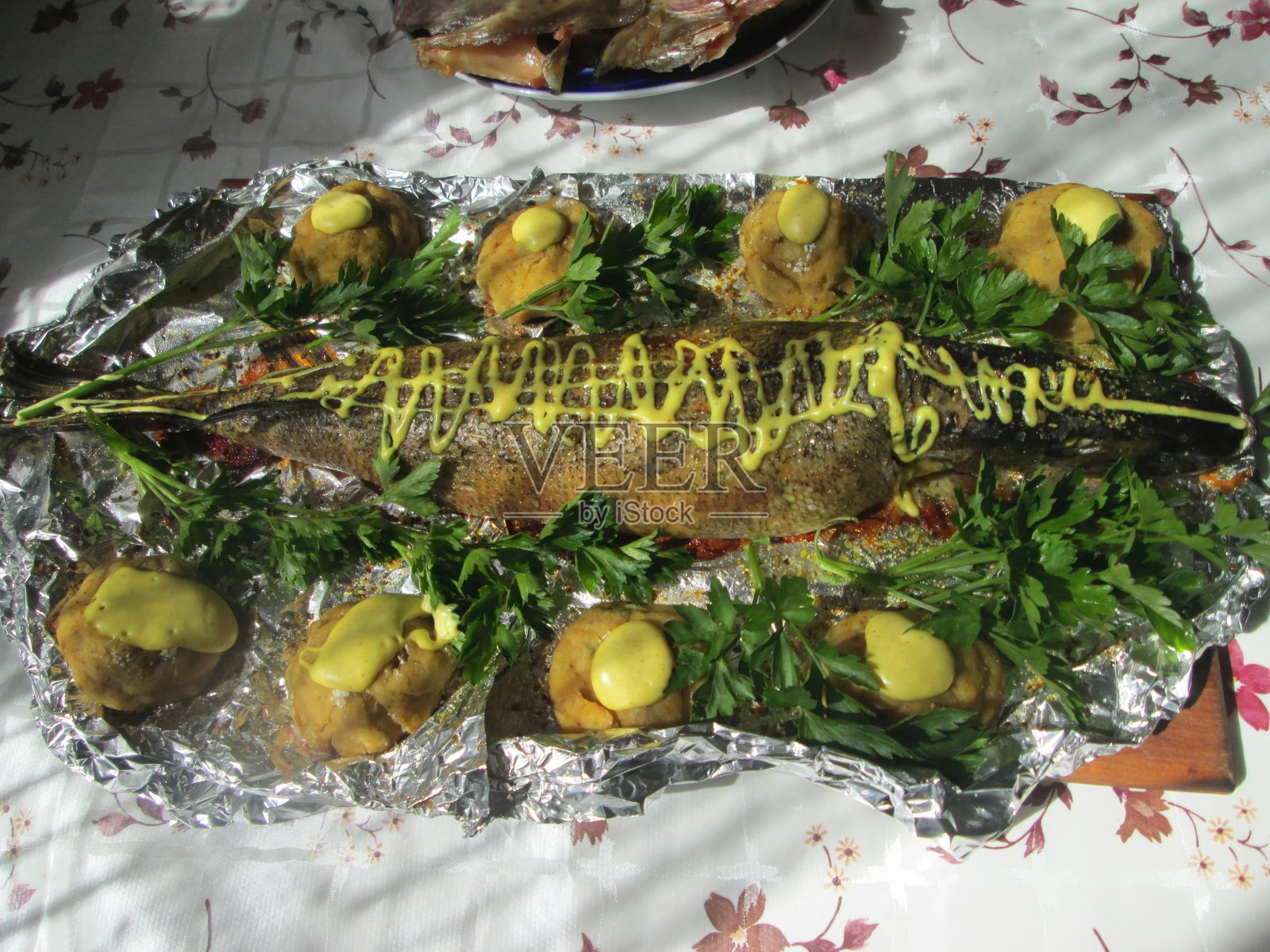 这道菜以整条鱼为特色，用香菜和芥末精心调味，配上金色的土豆，铺在花桌布上。照片摄影图片