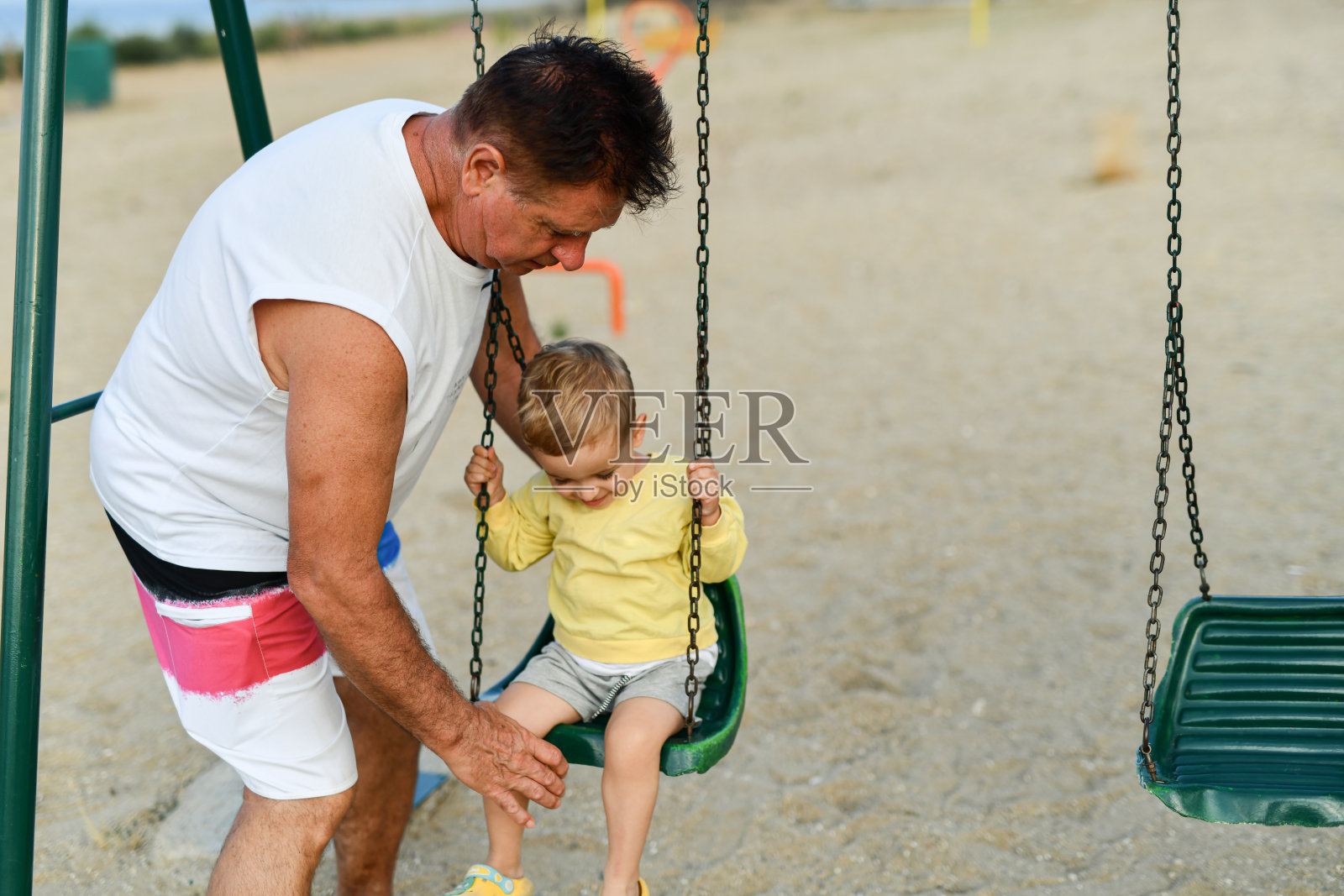 爷爷向蹒跚学步的男孩介绍游乐场秋千照片摄影图片